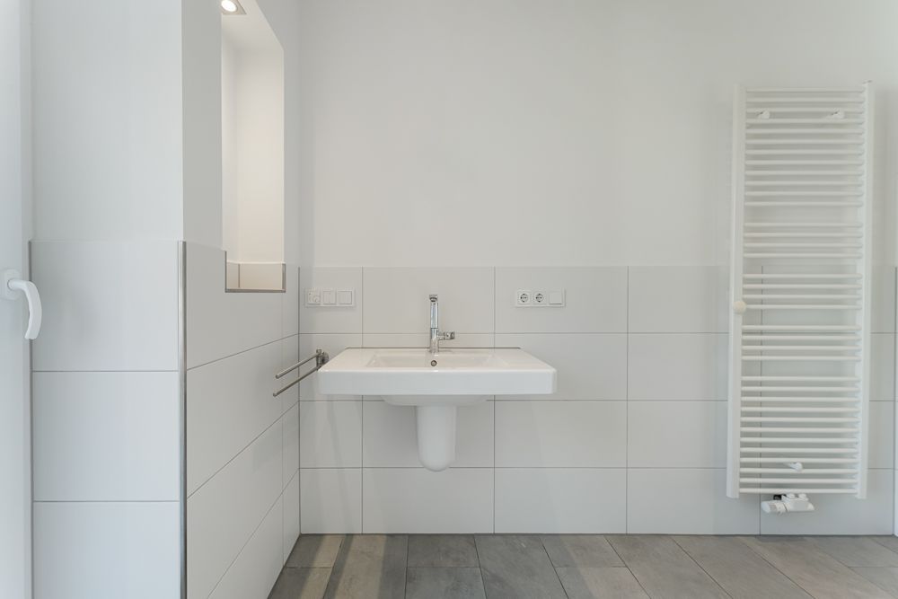 Modernes Badezimmer mit weißem Waschbecken, Spiegel und Handtuchheizkörper.