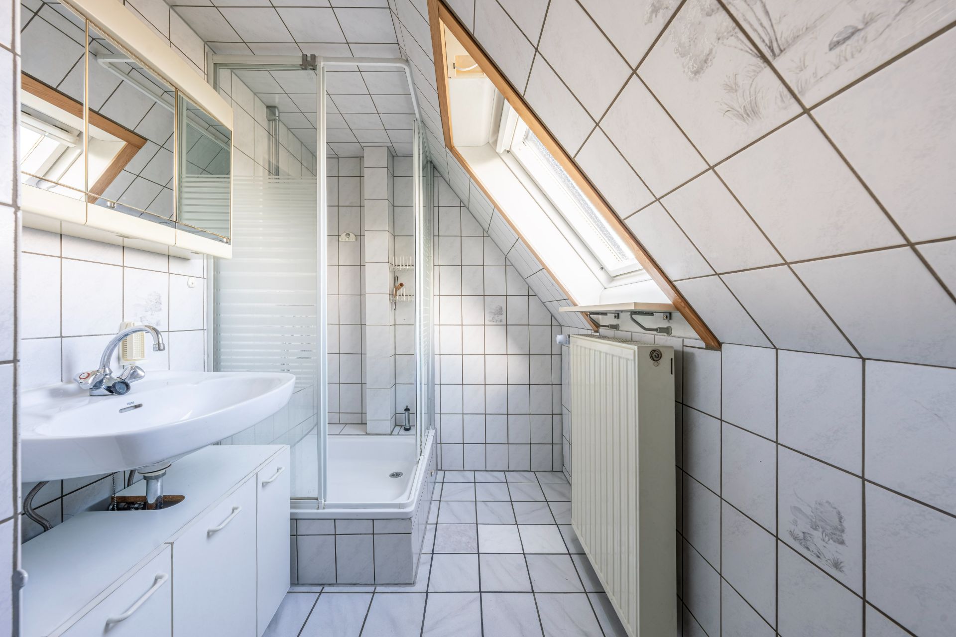 Helles Badezimmer mit Dusche, Waschbecken, Spiegel und Dachfenster, alles in weißen Fliesen.
