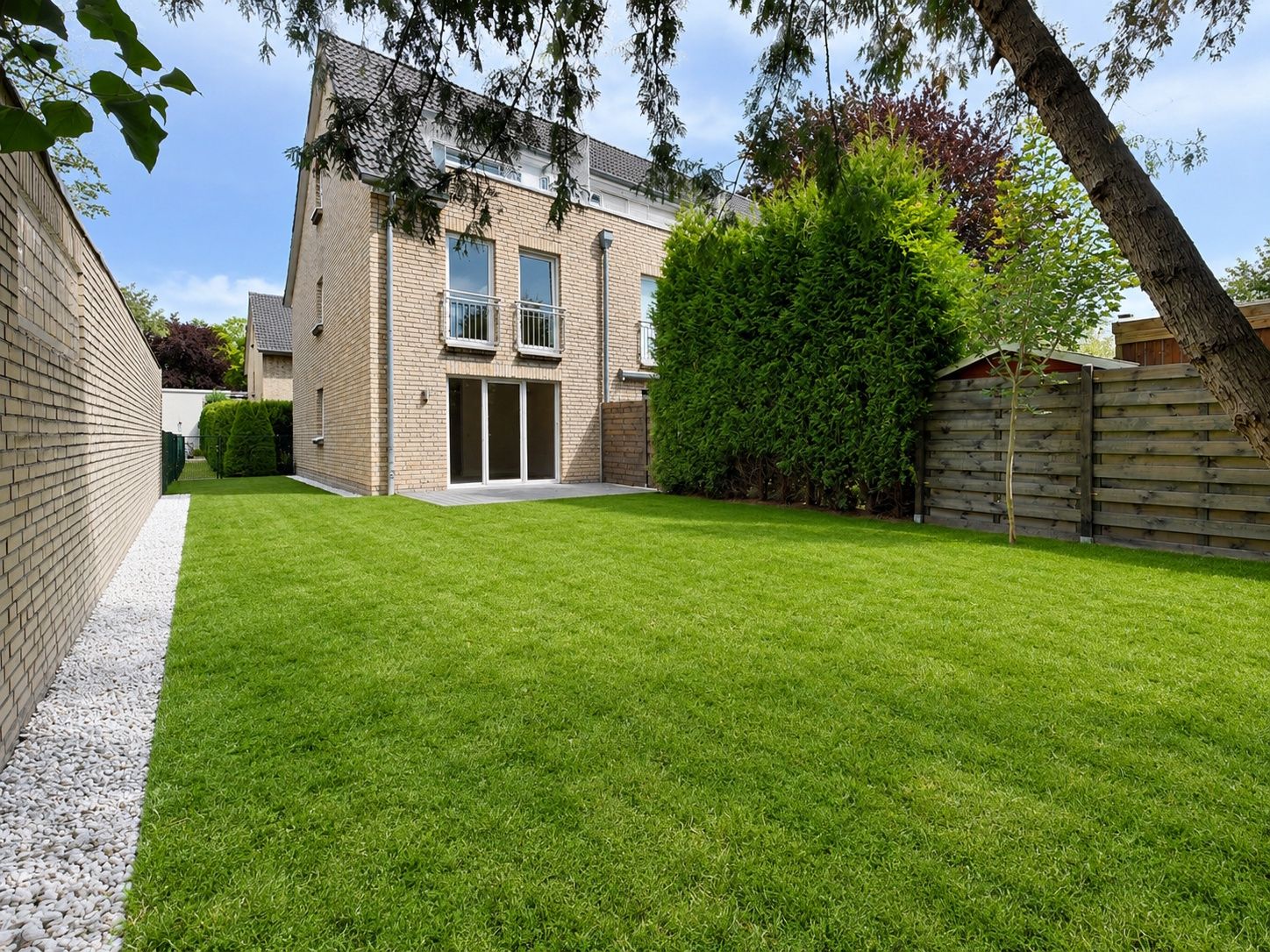 Gepflegter Garten mit Rasen, Hecke und Terrasse an einem modernen Wohnhaus.