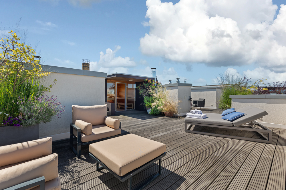 Möblierte Dachterrasse mit Sitzgruppe, Liege und Pflanzen bei sonnigem Wetter.