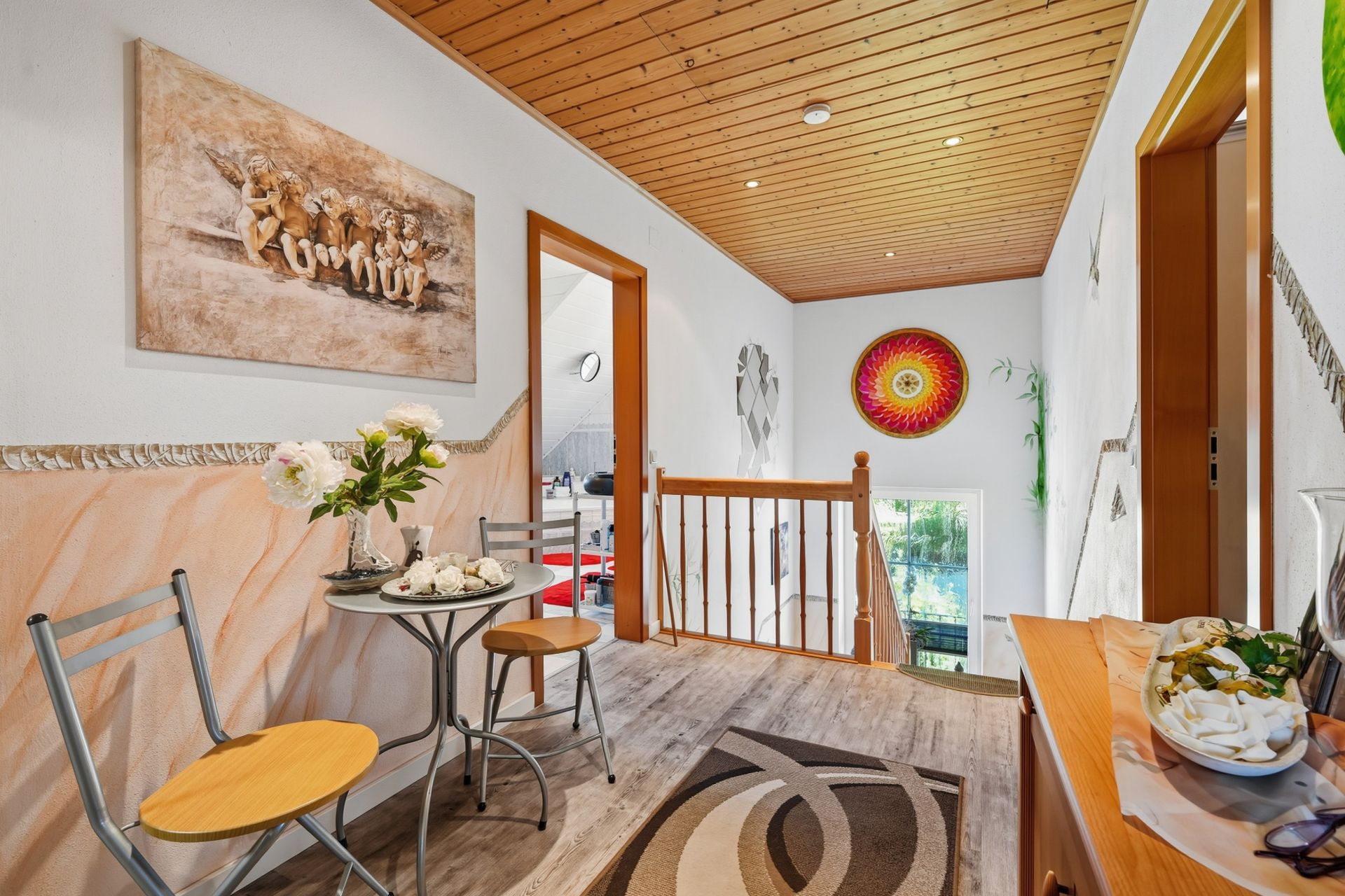 Heller Flur mit Holzdecke, kleiner Sitzecke, Teppich und Treppengeländer.