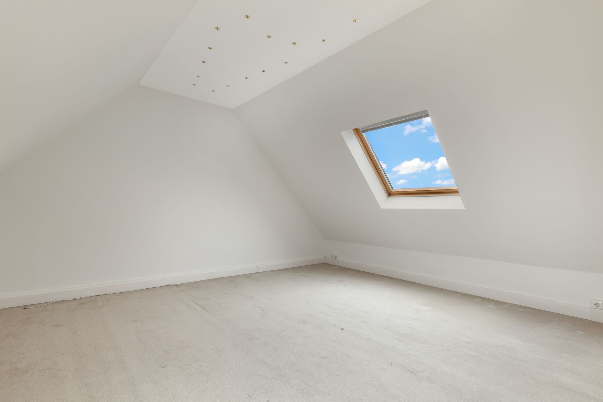 Leerer Dachbodenraum mit weiß gestrichenen Wänden und Dachflächenfenster.