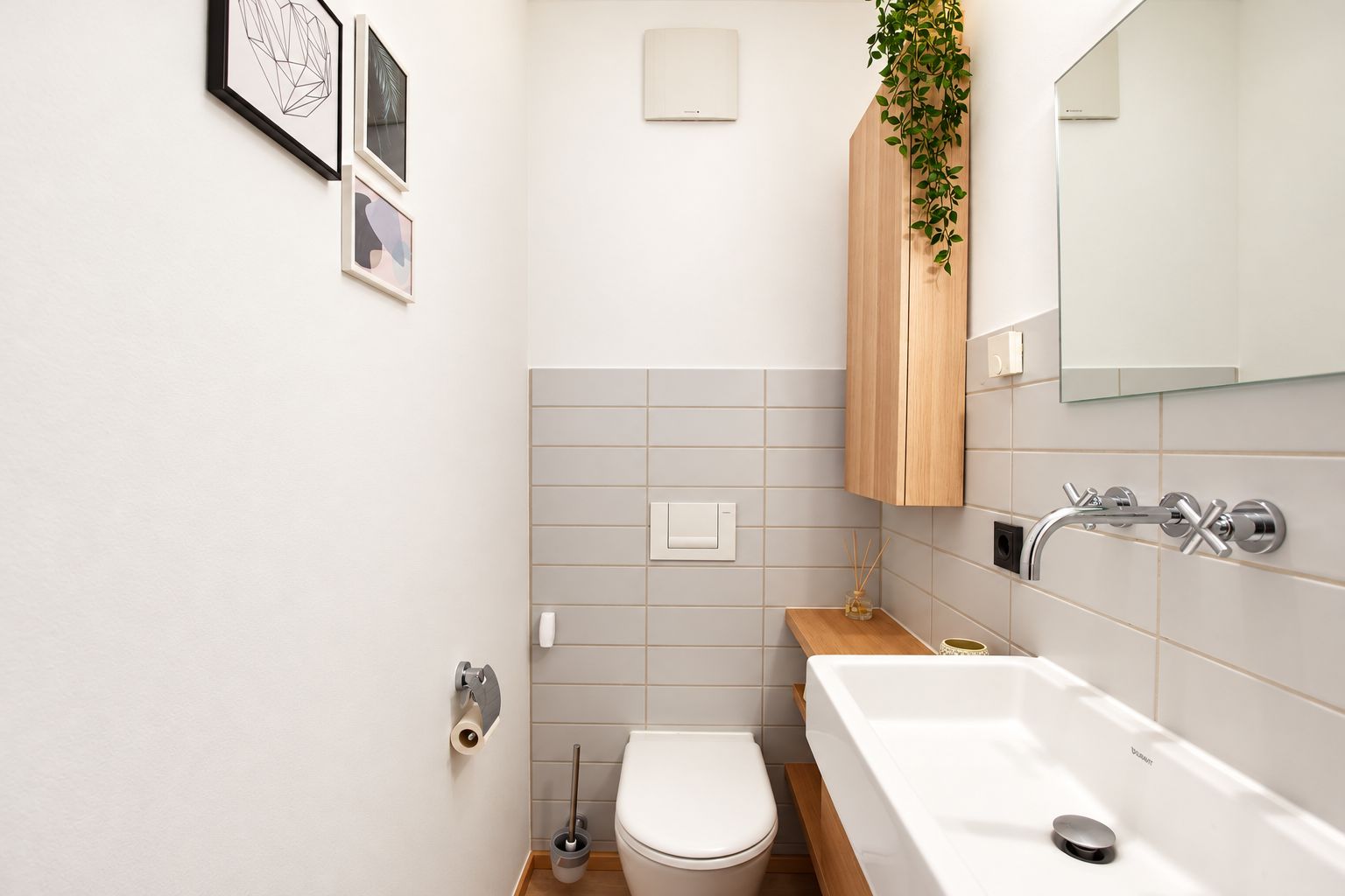 Modernes, schmales Badezimmer mit Toilette, Waschbecken, Wandspiegel und Holzschrank.