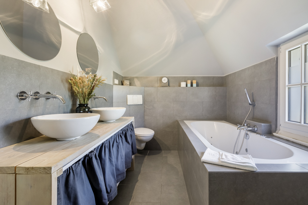 Modernes Badezimmer mit zwei Waschbecken, Badewanne, WC und großen Spiegeln.