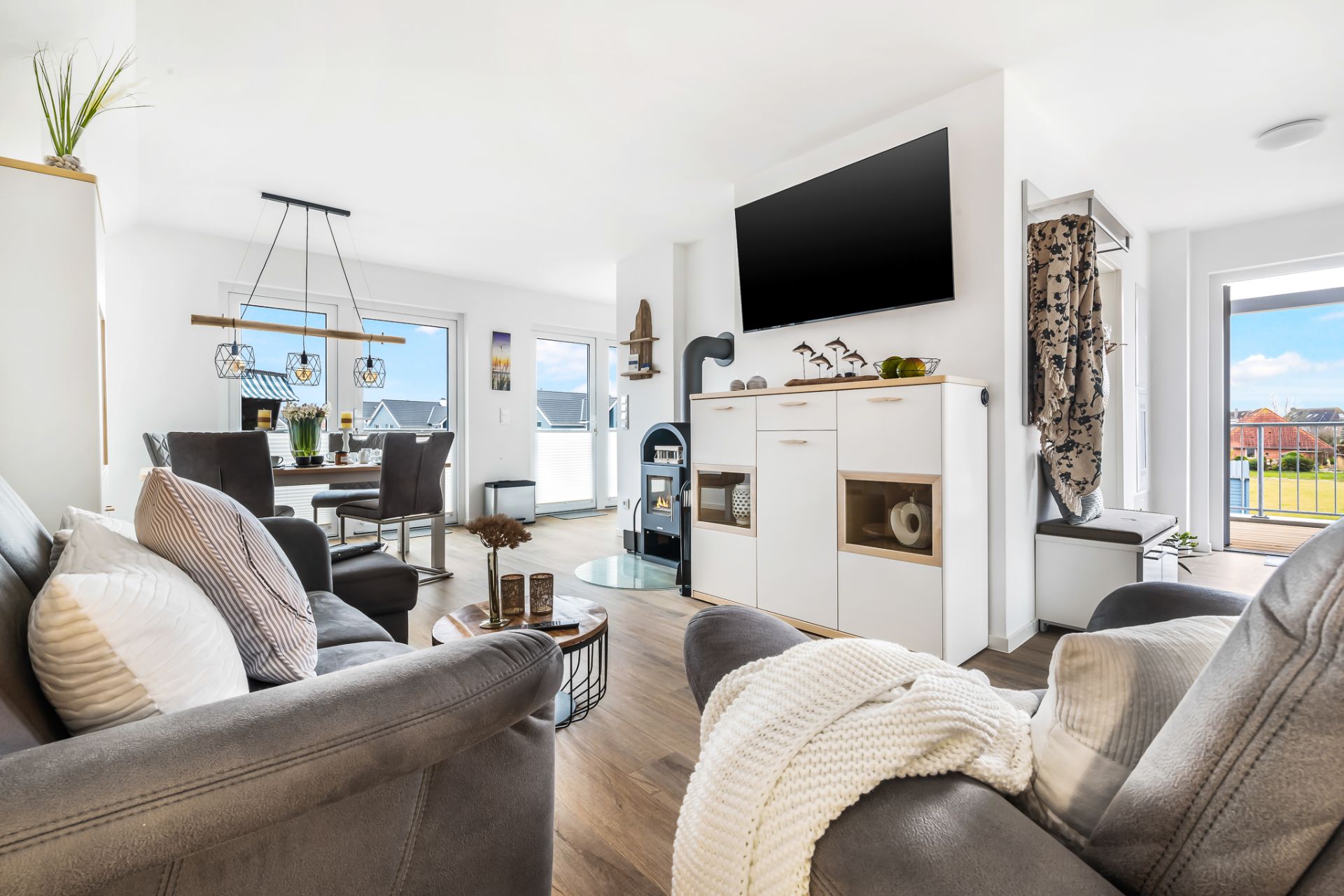 Modernes Wohnzimmer mit Sofa, Esstisch, Fernseher und großen Fenstern mit Blick nach draußen.