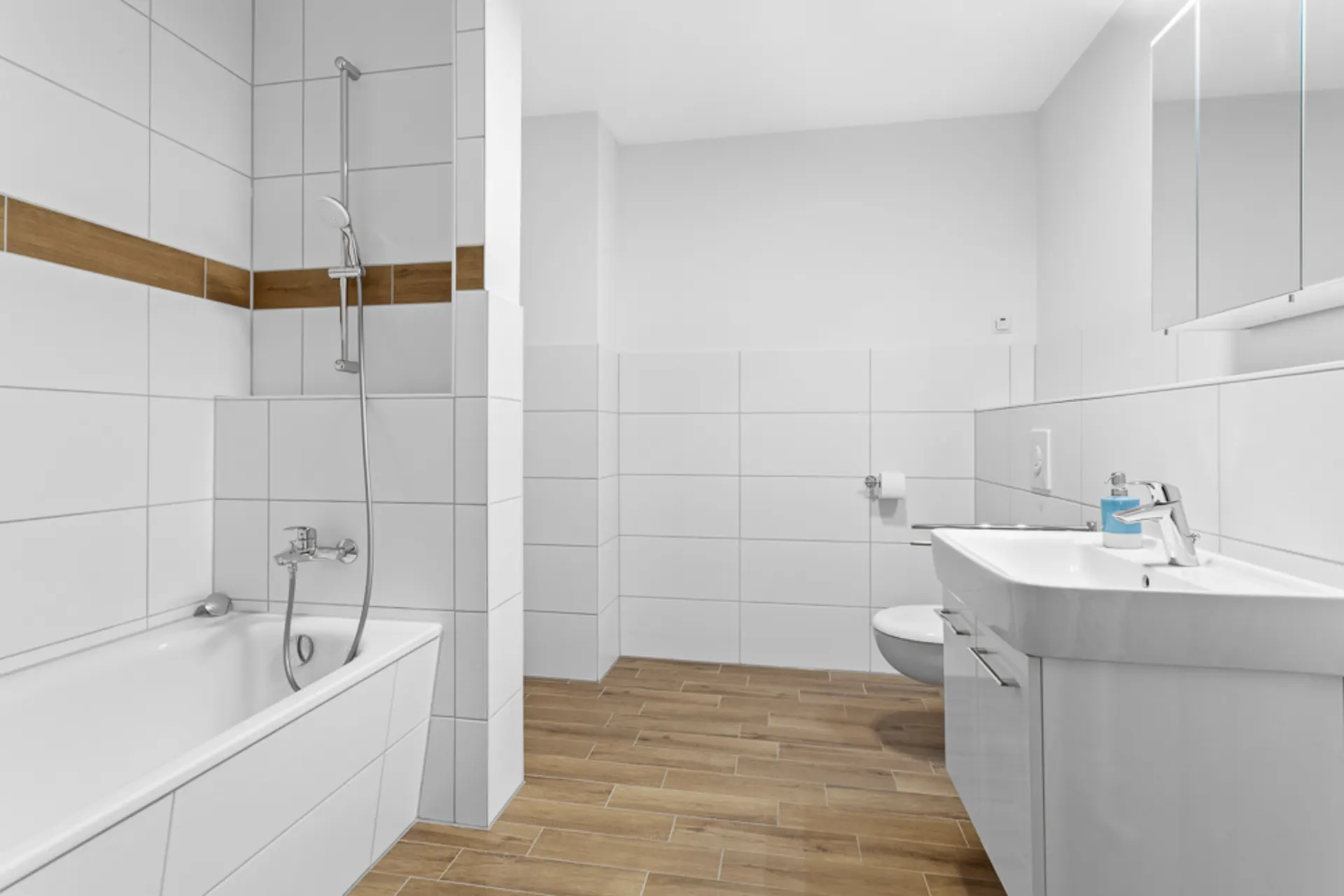 Modernes Badezimmer mit Badewanne, Duschkopf, Waschbecken und WC auf Holzfliesenboden.