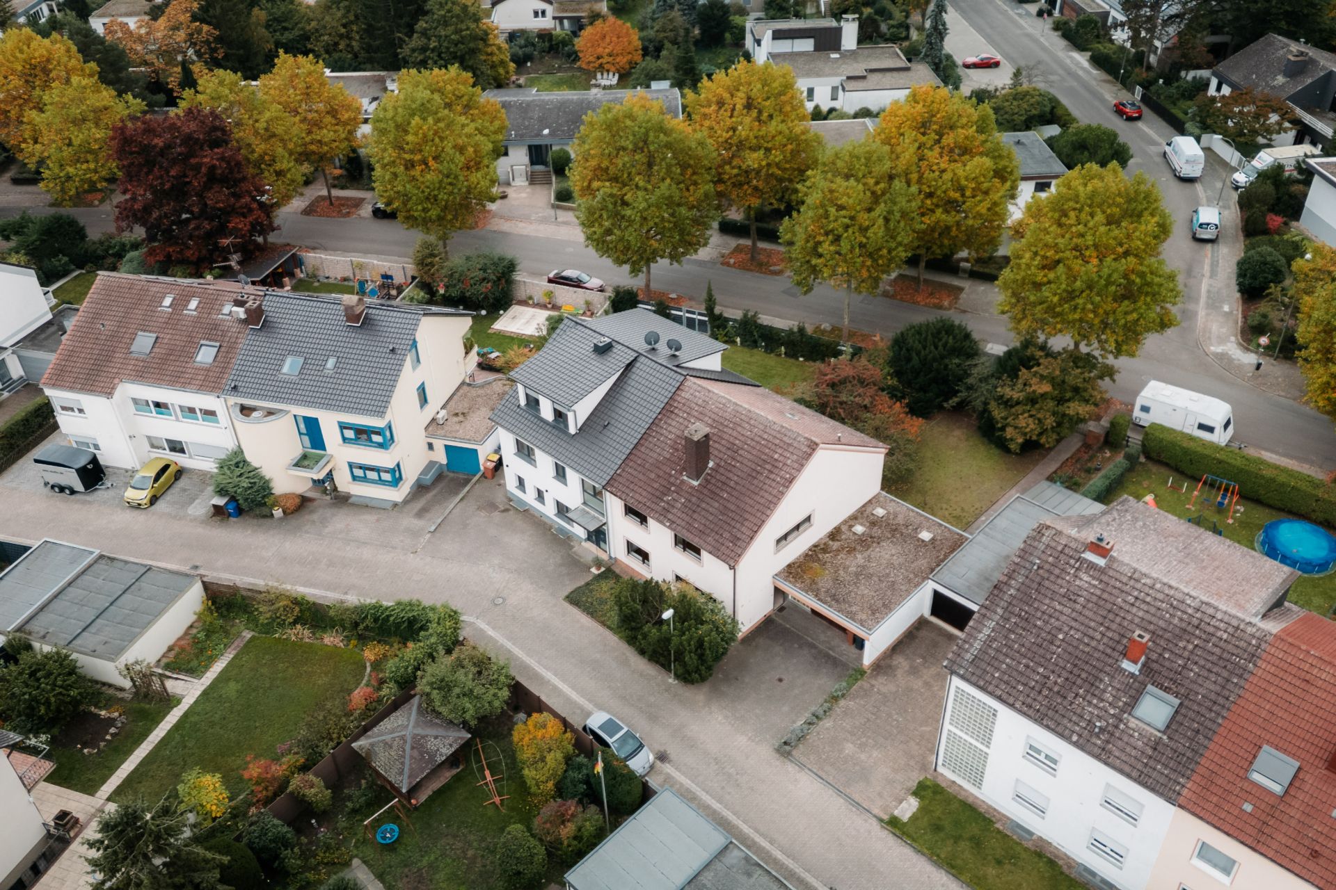 Luftaufnahme von Wohnhäusern mit Vorgärten und Bäumen an einer ruhigen Straße.