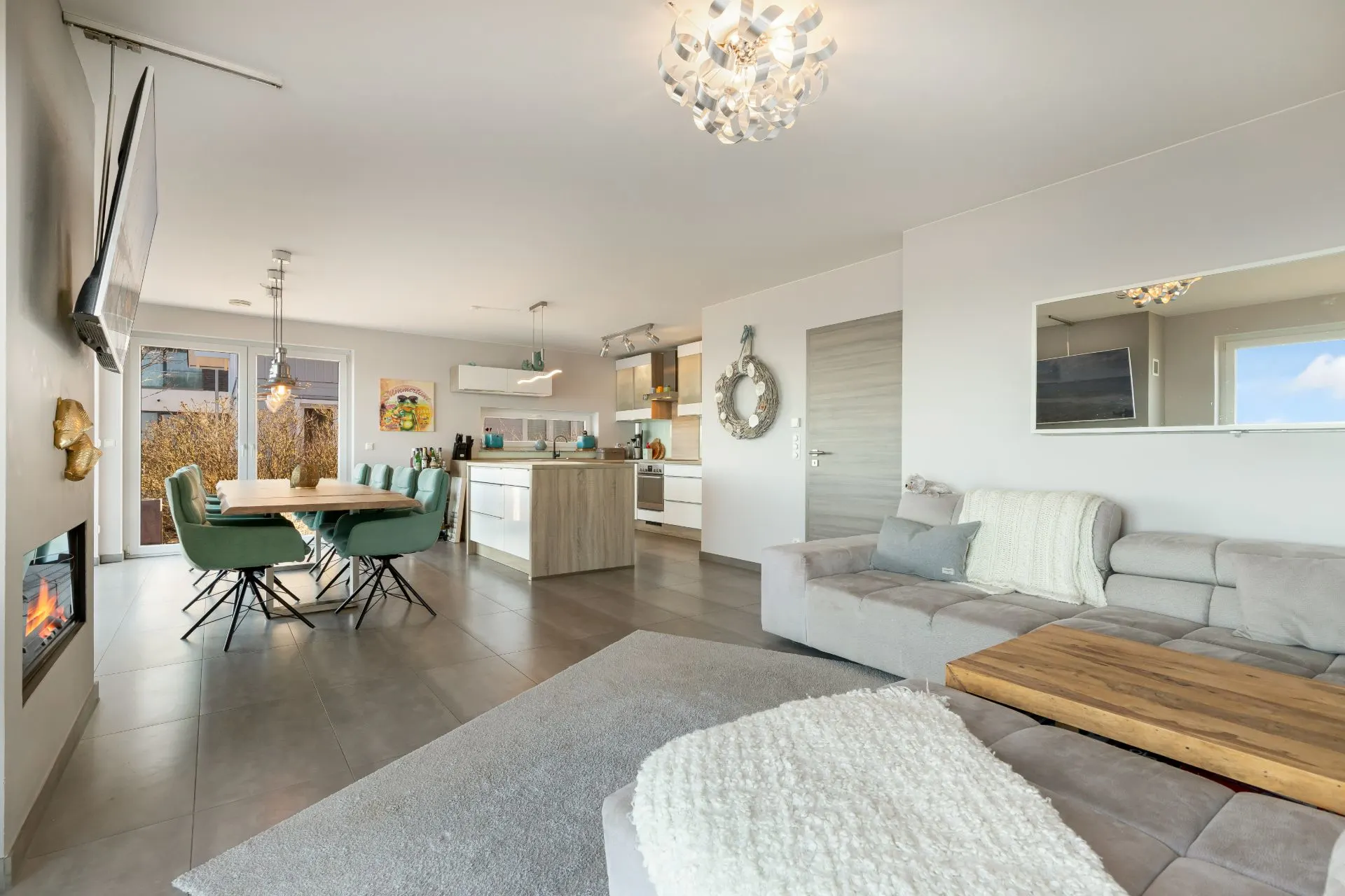Modernes Wohnzimmer mit grauem Sofa, Essbereich und offener Küche, helle und gemütliche Atmosphäre.