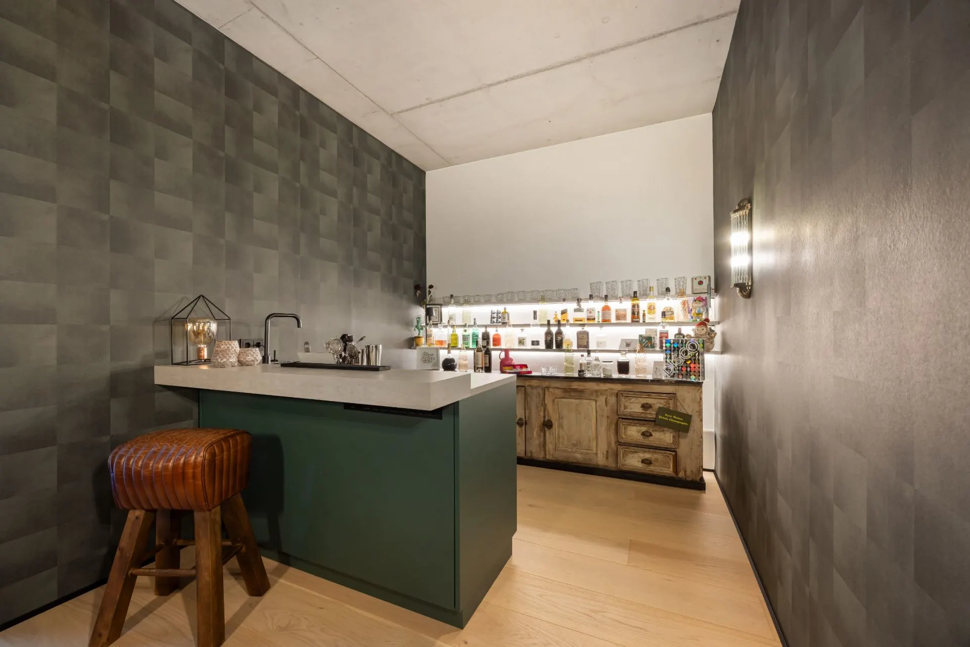 Moderne Hausbar mit Tresen, Hocker und beleuchteten Regalen mit Flaschen an der Wand.