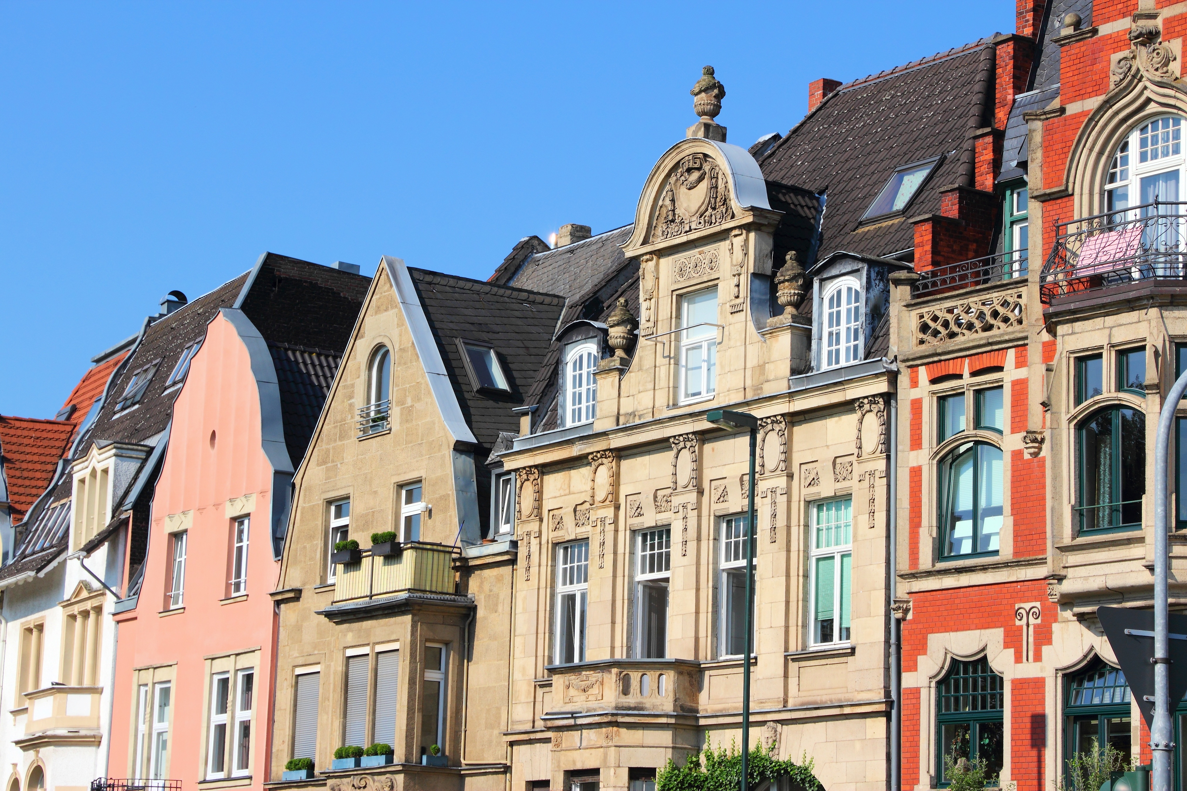 Mehrere bunte Wohnhäuser mit historischen Fassaden und Dachgauben bei blauem Himmel.
