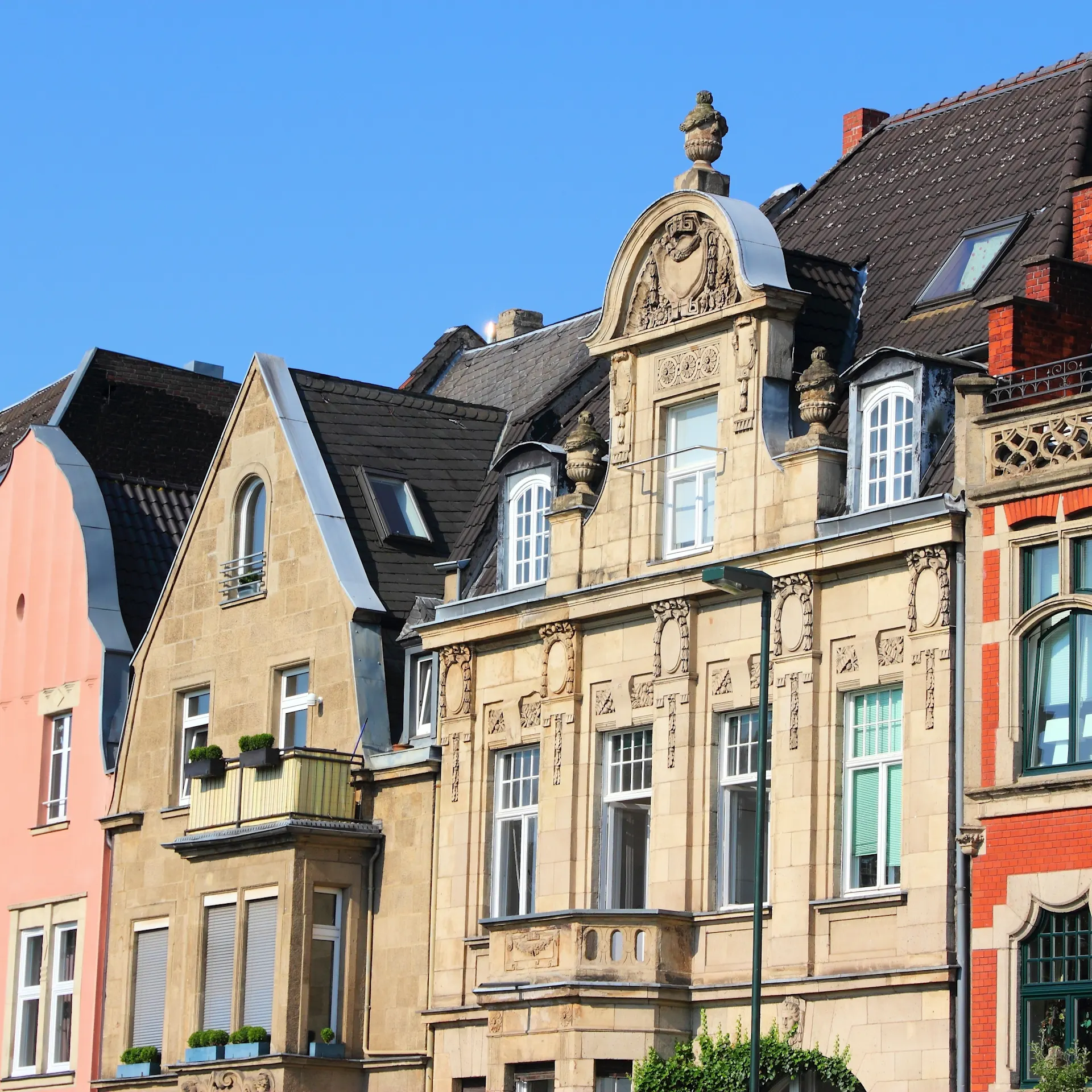 Mehrere bunte Wohnhäuser mit historischen Fassaden und Dachgauben bei blauem Himmel.