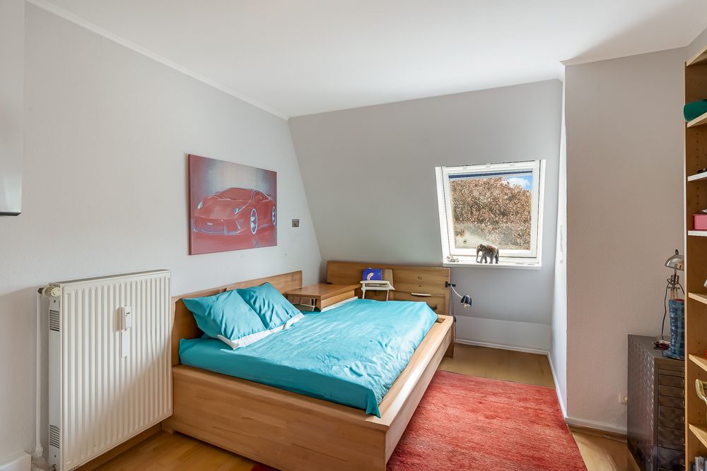 Schlafzimmer mit Holzbett, türkisfarbener Bettwäsche und Fenster. Bild eines roten Autos an der Wand.