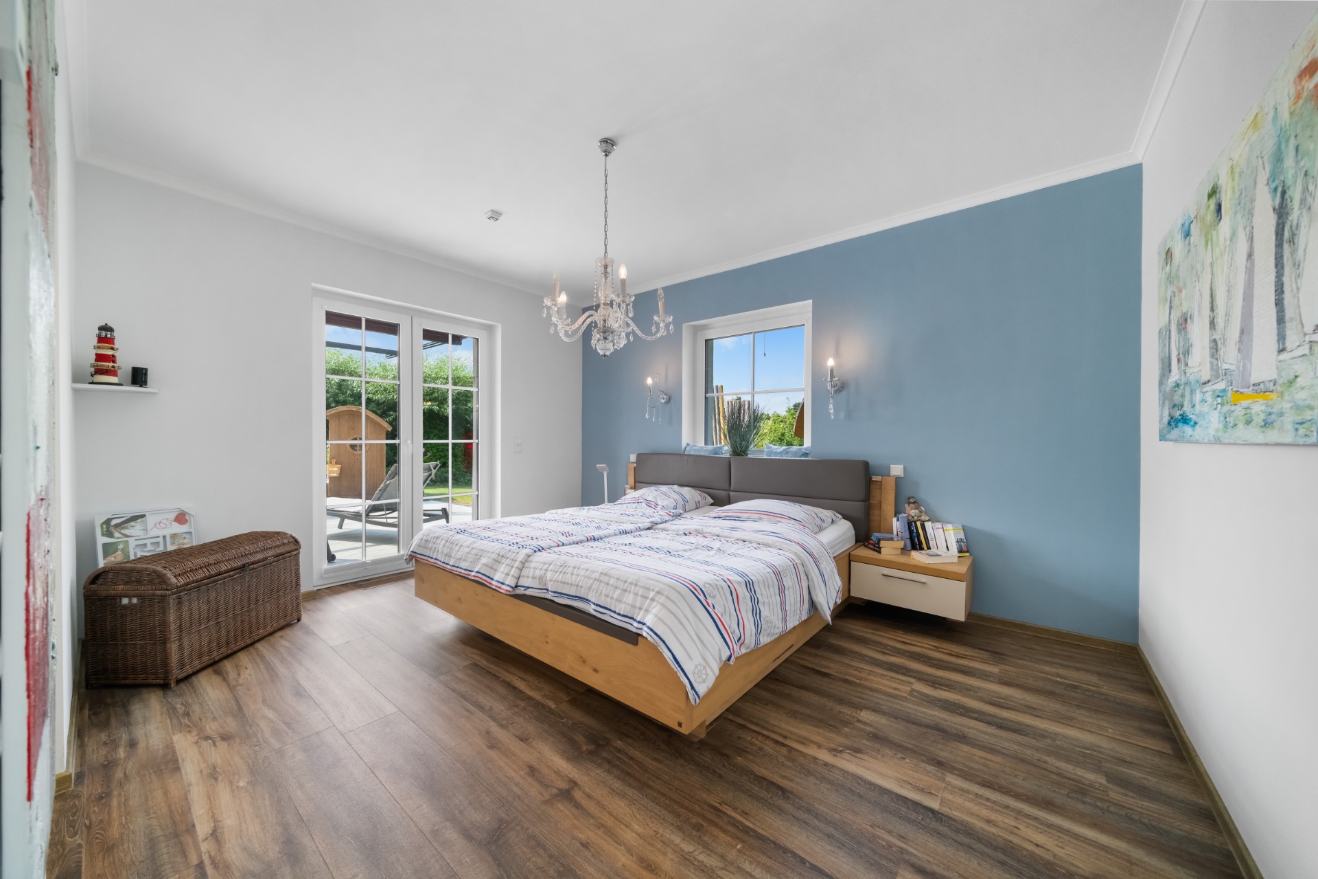 Helles Schlafzimmer mit Doppelbett, Holzboden, Fenster, Tür zur Terrasse und blauer Akzentwand.