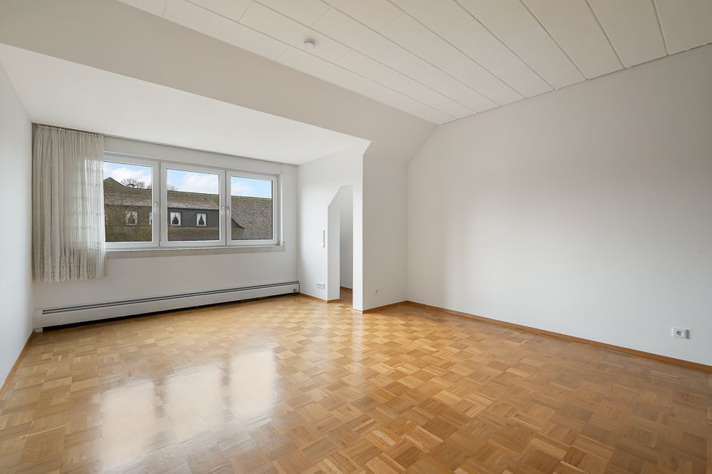 Helles, leeres Zimmer mit Parkettboden, weißen Wänden und großem Fenster.
