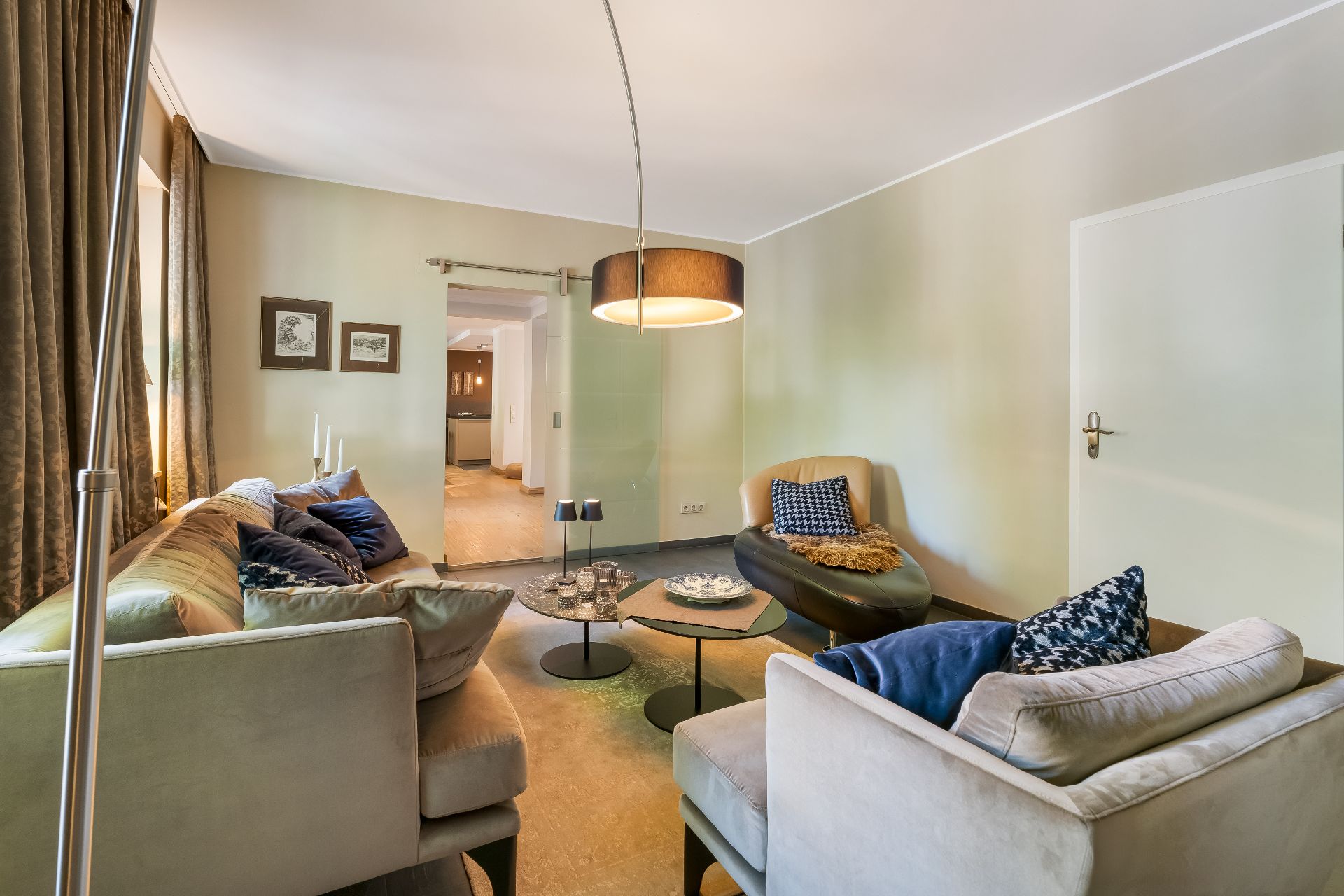 Helles Wohnzimmer mit Sofas, Sesseln, Couchtischen und großem Deckenlicht.