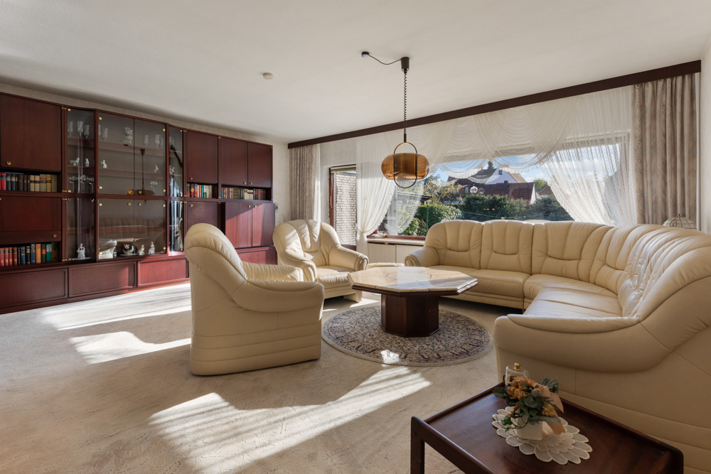Helles Wohnzimmer mit cremefarbenen Ledersofas, großem Fenster und Holzregalwand mit Büchern.