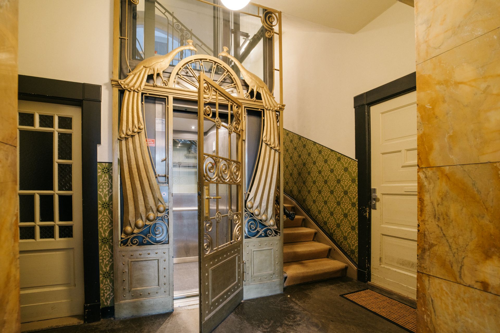 Eingangsbereich mit verziertem Aufzug und Treppe in einem Wohnhaus.
