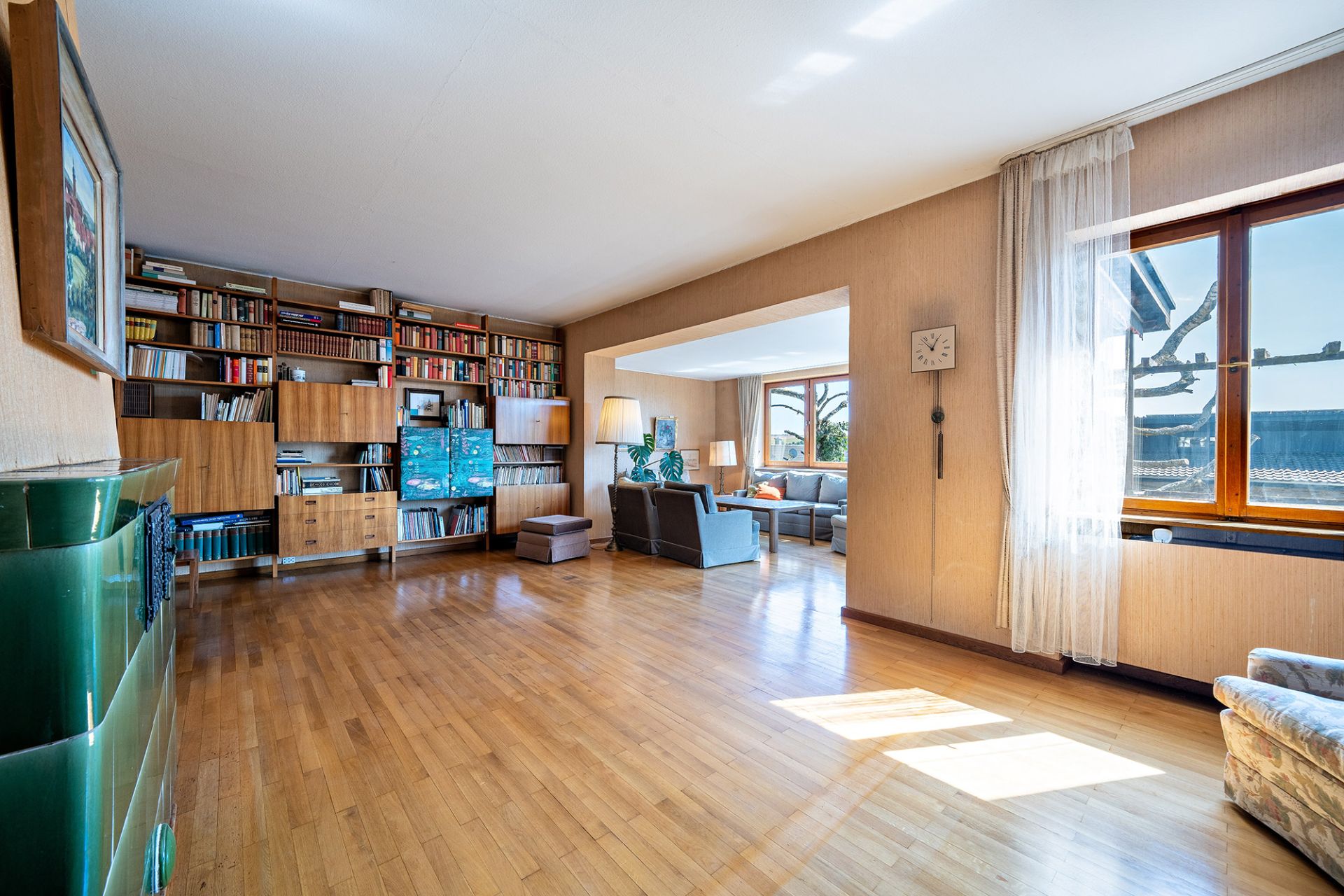 Helles Wohnzimmer mit Holzfußboden, Bücherregal, Sofa und großen Fenstern.