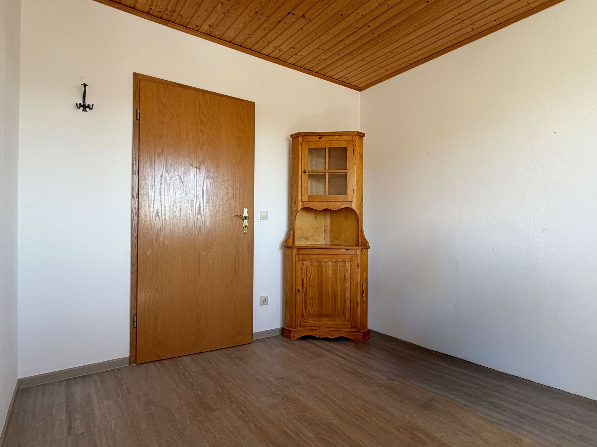 Leeres Zimmer mit Holztür und Holzschrank in der Ecke, Holzdecke und Laminatboden.