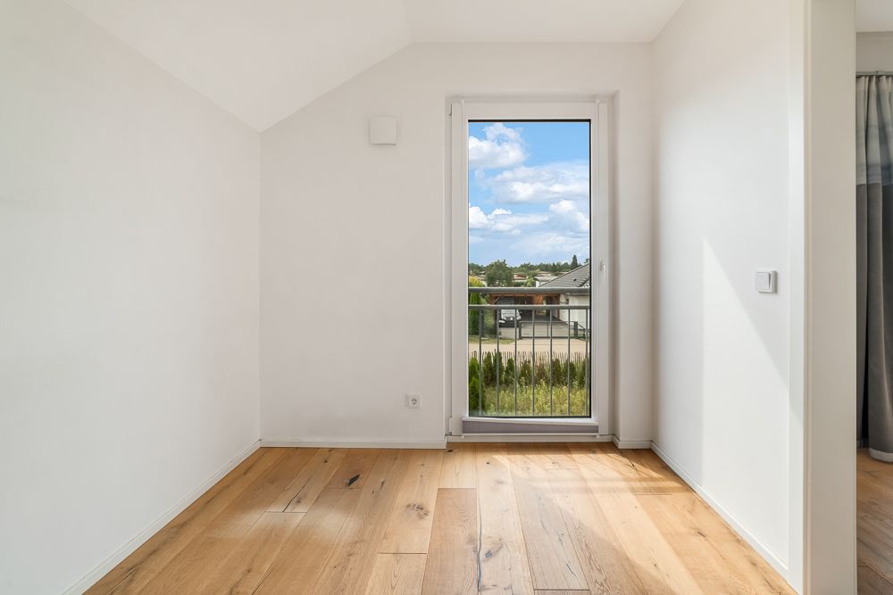 Leerer Raum mit hellem Holzboden und Glastür mit Blick nach draußen.