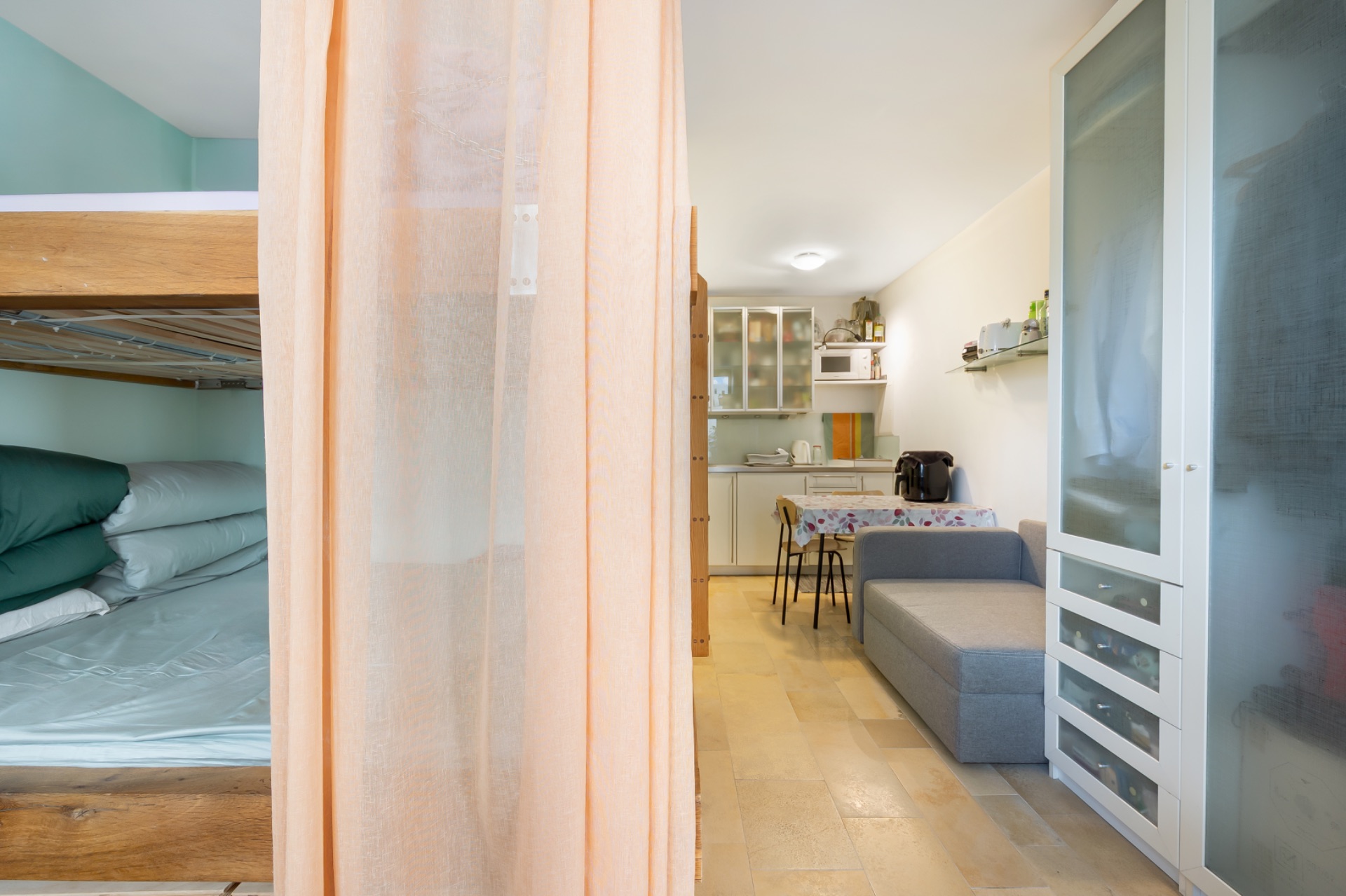Kleine Wohnung mit Etagenbett, Vorhang, Sofa, Esstisch und Küchenzeile.