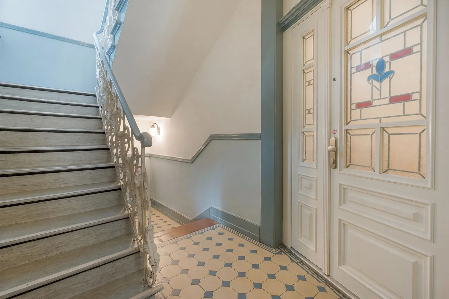 Treppenhaus mit verzierten Geländer und Tür mit buntem Glasfenster.