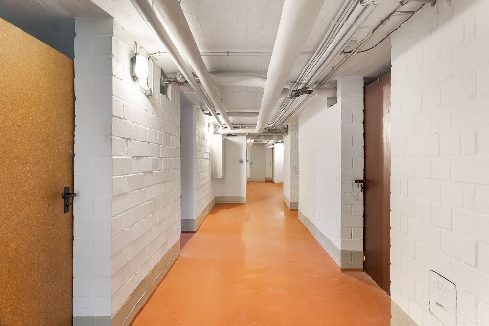 Heller Flur mit weißen Wänden, Rohren an der Decke und mehreren Türen.