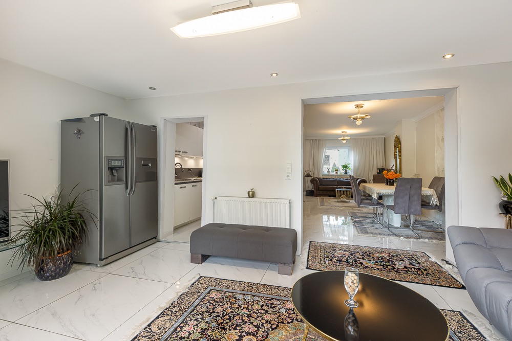 Helles Wohnzimmer mit Sofa, Teppichen, großem Kühlschrank und Blick ins Esszimmer.