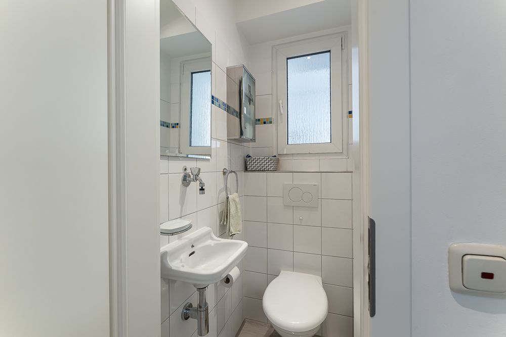 Kleines Badezimmer mit WC, Waschbecken, Spiegel und Fenster.