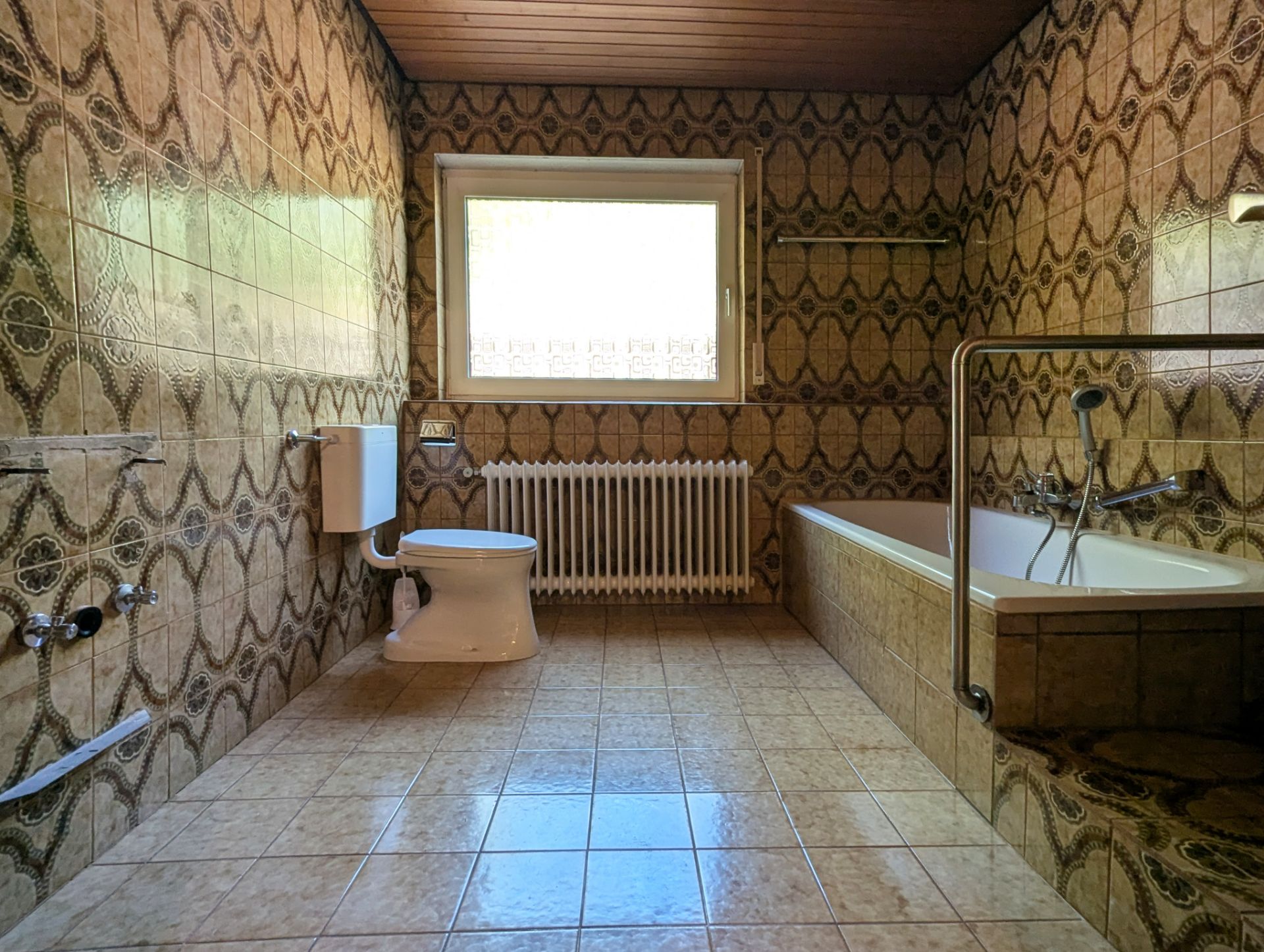 Badezimmer mit gemusterten Fliesen, Toilette, Badewanne und großem Fenster.