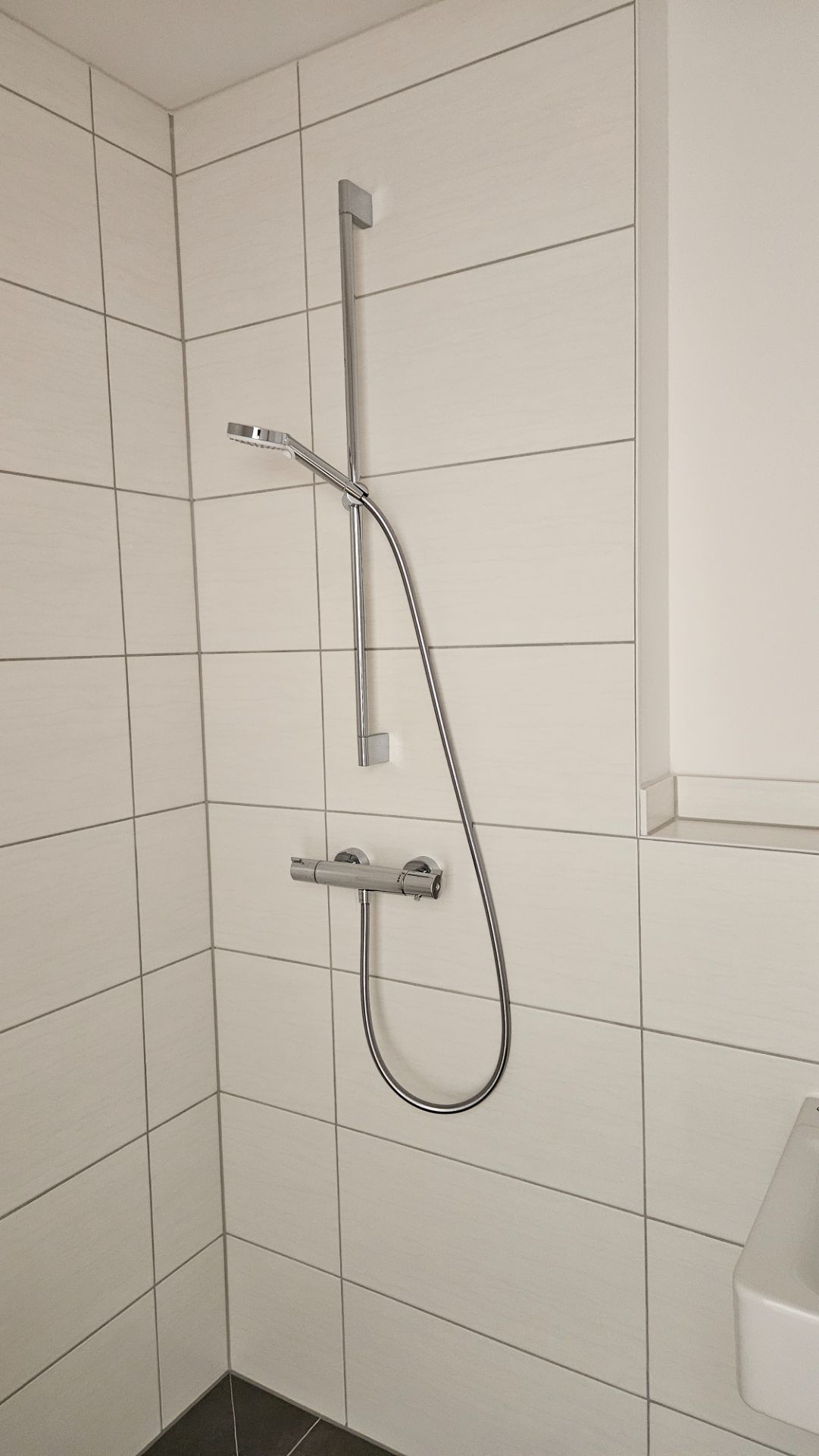 Moderne Dusche mit heller Fliesenwand und verstellbarem Duschkopf.