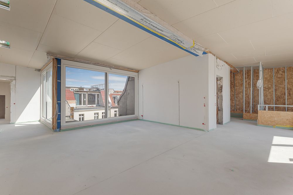 Heller, unfertiger Wohnraum mit großen Fenstern und Blick auf Nachbarhäuser.