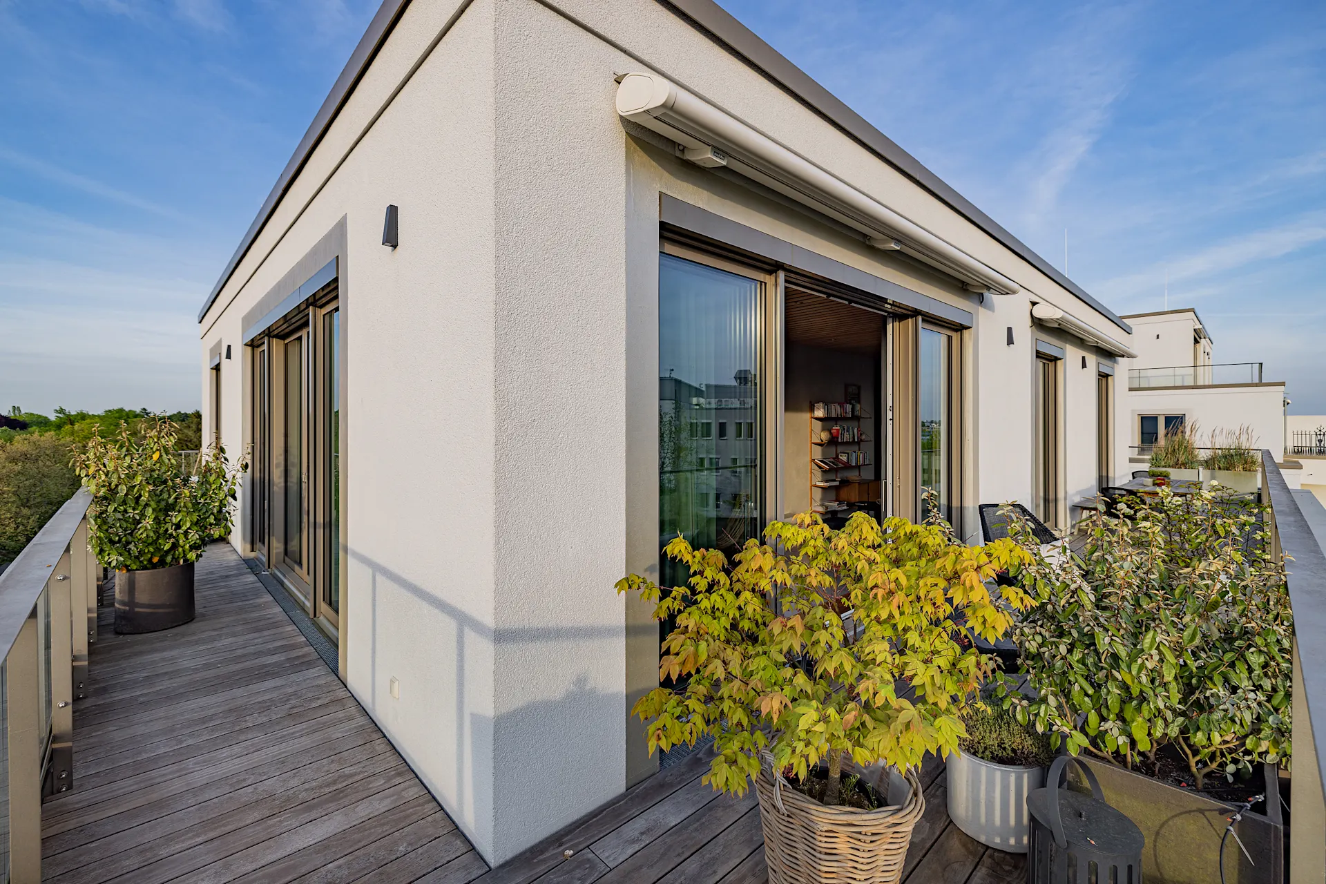 Moderne Dachterrasse mit großen Fenstern, Pflanzen in Töpfen und Holzboden.