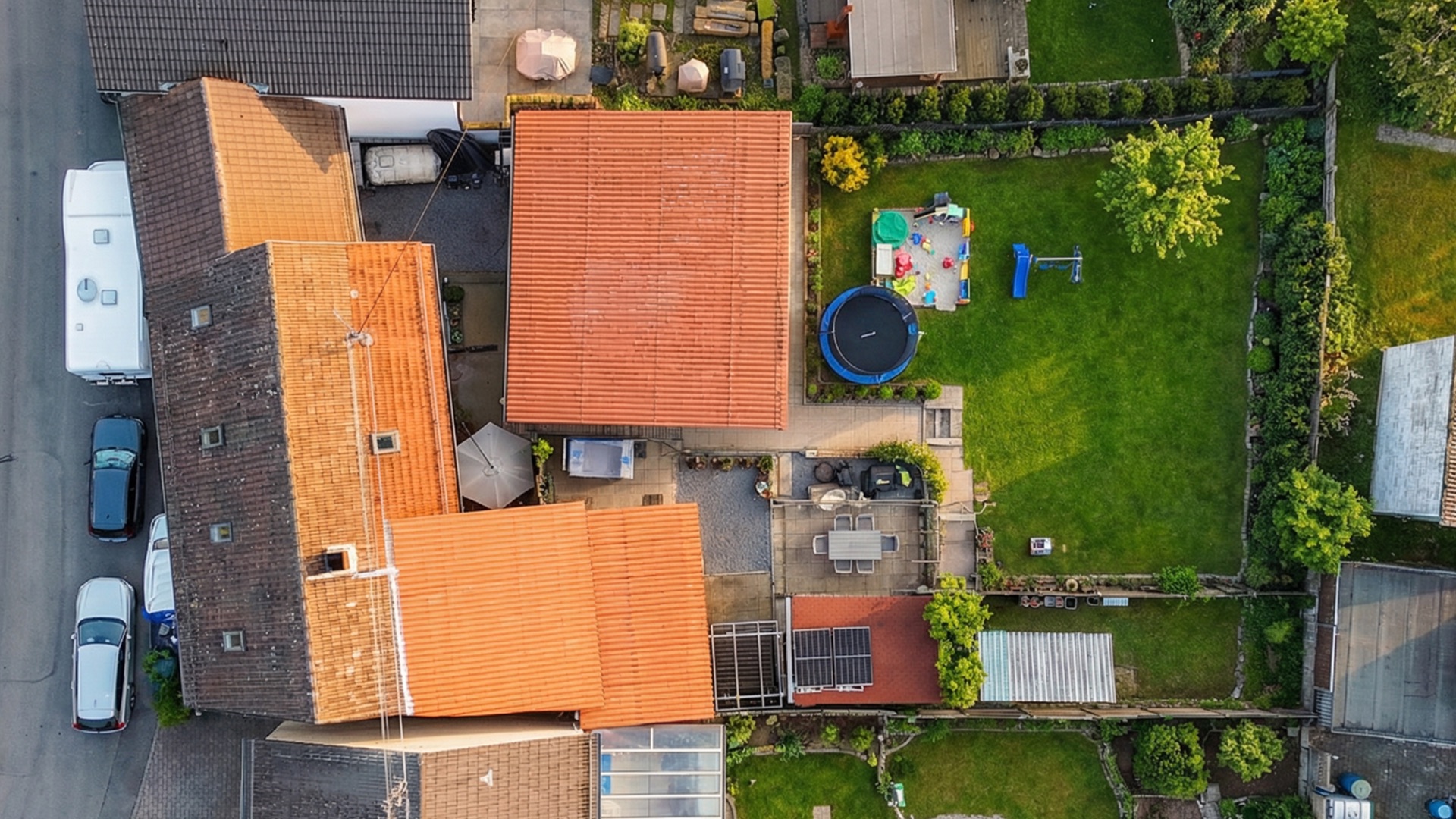 Luftaufnahme eines Wohnhauses mit Garten, Trampolin und Spielplatz im Hinterhof.