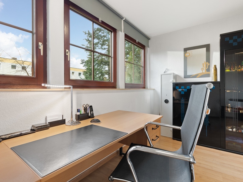Modernes Arbeitszimmer mit Schreibtisch, Bürostuhl und drei großen Fenstern.