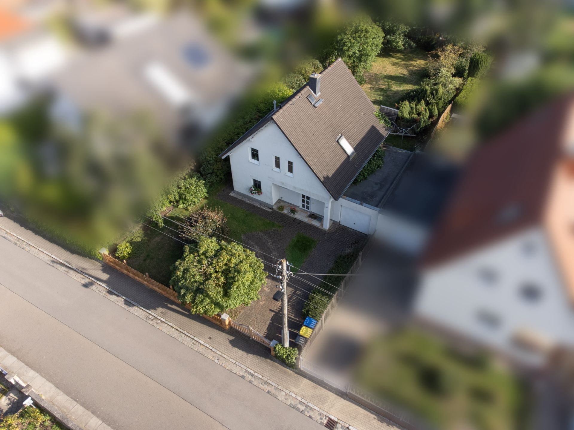 Luftaufnahme eines Einfamilienhauses mit Garten an einer ruhigen Straße.