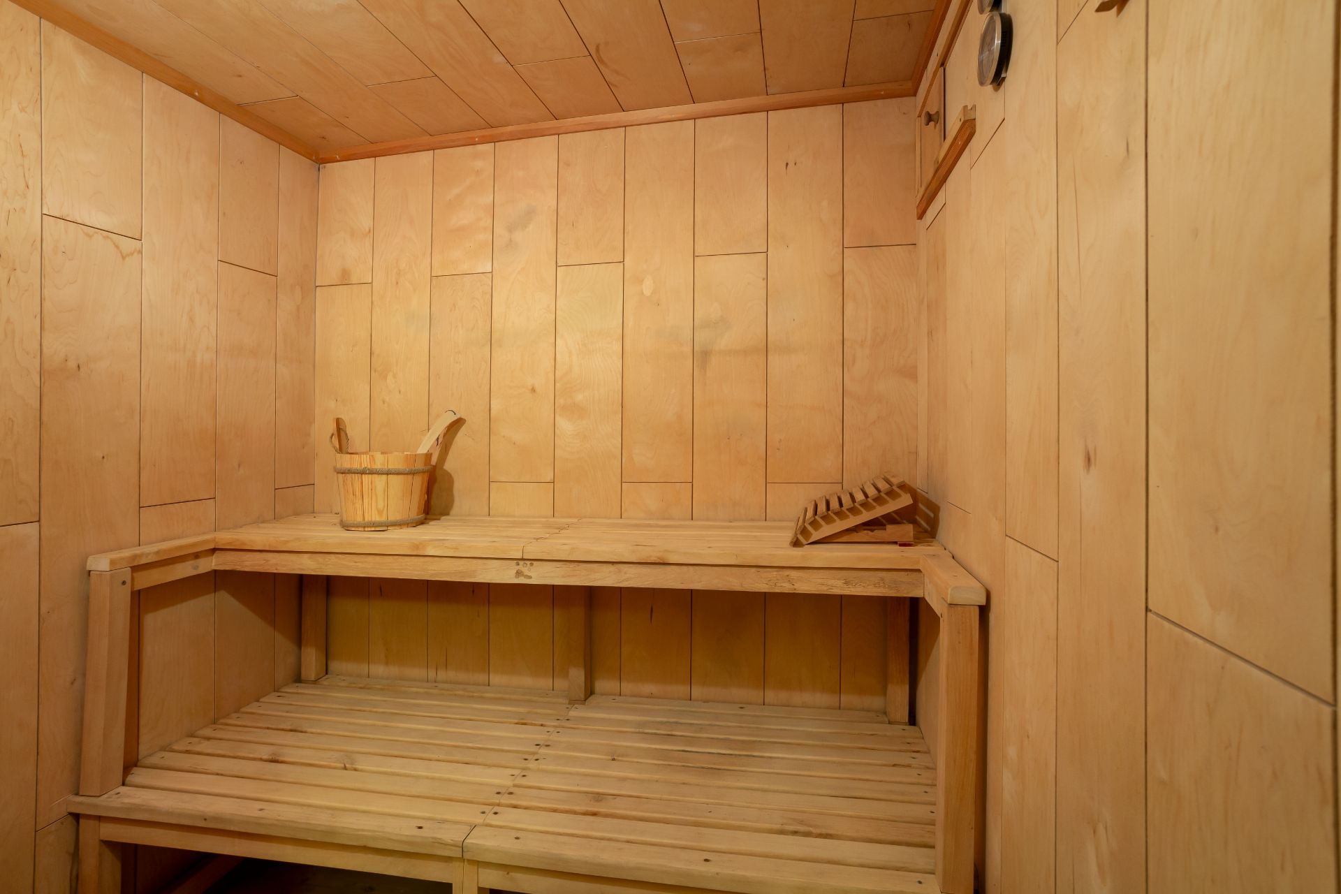 Holzsauna mit zwei Bänken, einem Eimer und einer Kopfstütze.