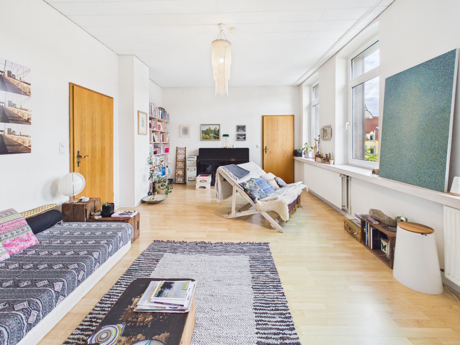 Helles Wohnzimmer mit Sofa, Teppich, Couchtisch, Regalen und großen Fenstern.
