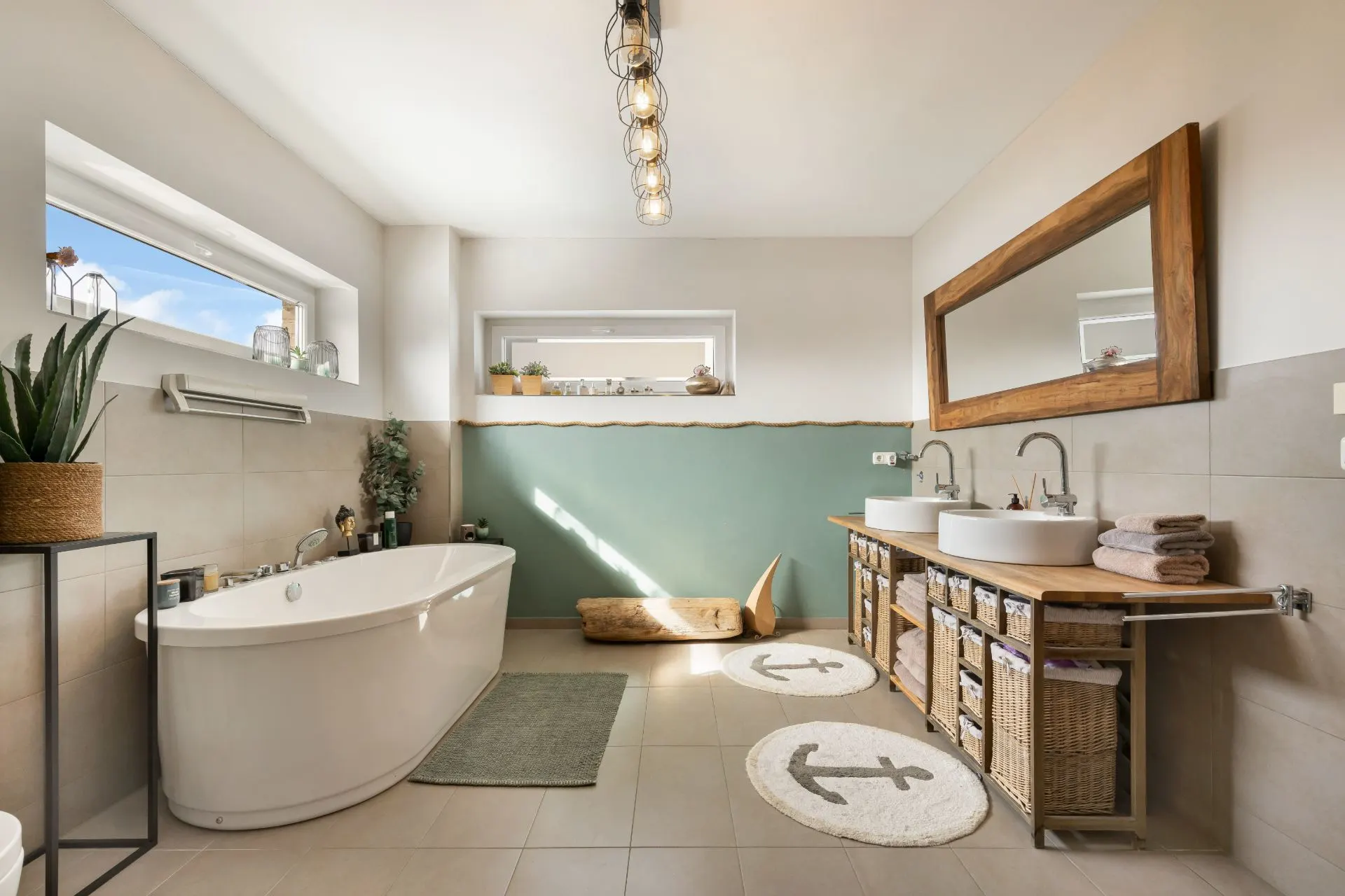Modernes Badezimmer mit Badewanne, Doppelwaschbecken, großem Spiegel und runden Teppichen mit Anker-Motiv.