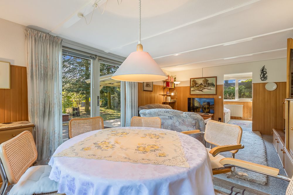 Helles Wohnzimmer mit Esstisch, Stühlen und Blick auf den Garten durch große Fenster.