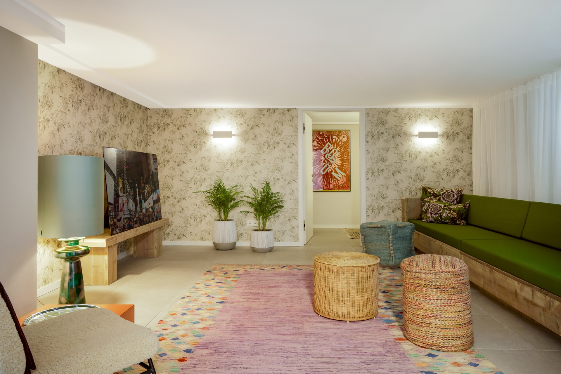 Wohnzimmer mit grüner Sofa, buntem Teppich, zwei Pflanzen und Wandbild, moderne Beleuchtung.