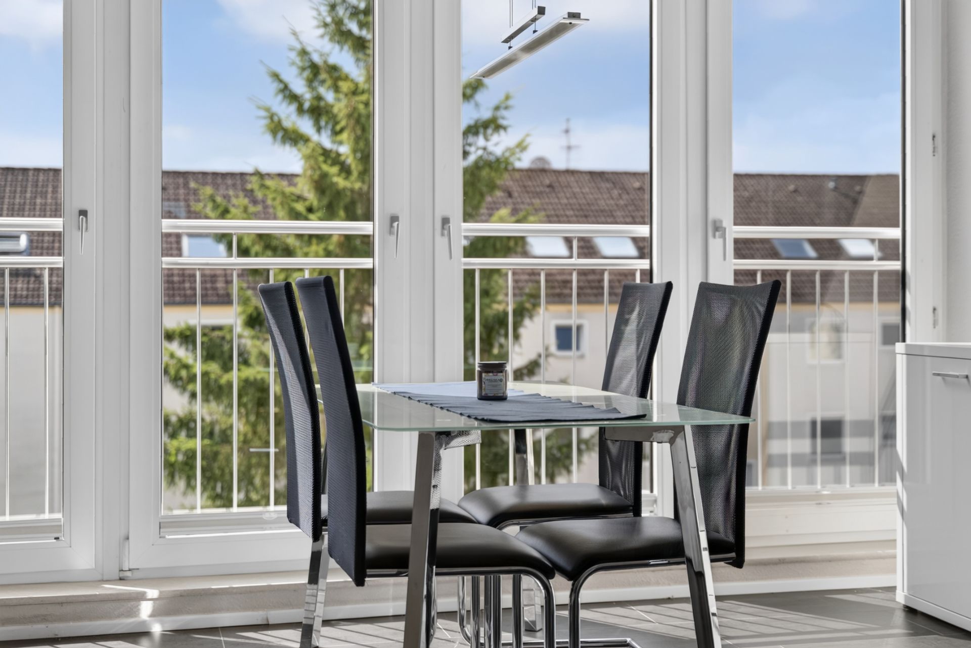 Essbereich mit Glastisch und vier schwarzen Stühlen vor großen Fenstern mit Blick nach draußen.