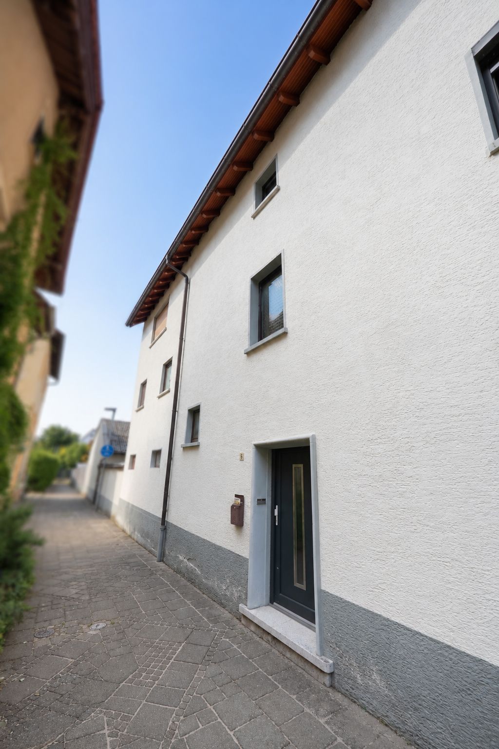 Hauseingang mit grauer Tür und mehreren Fenstern an einer weißen Fassade.