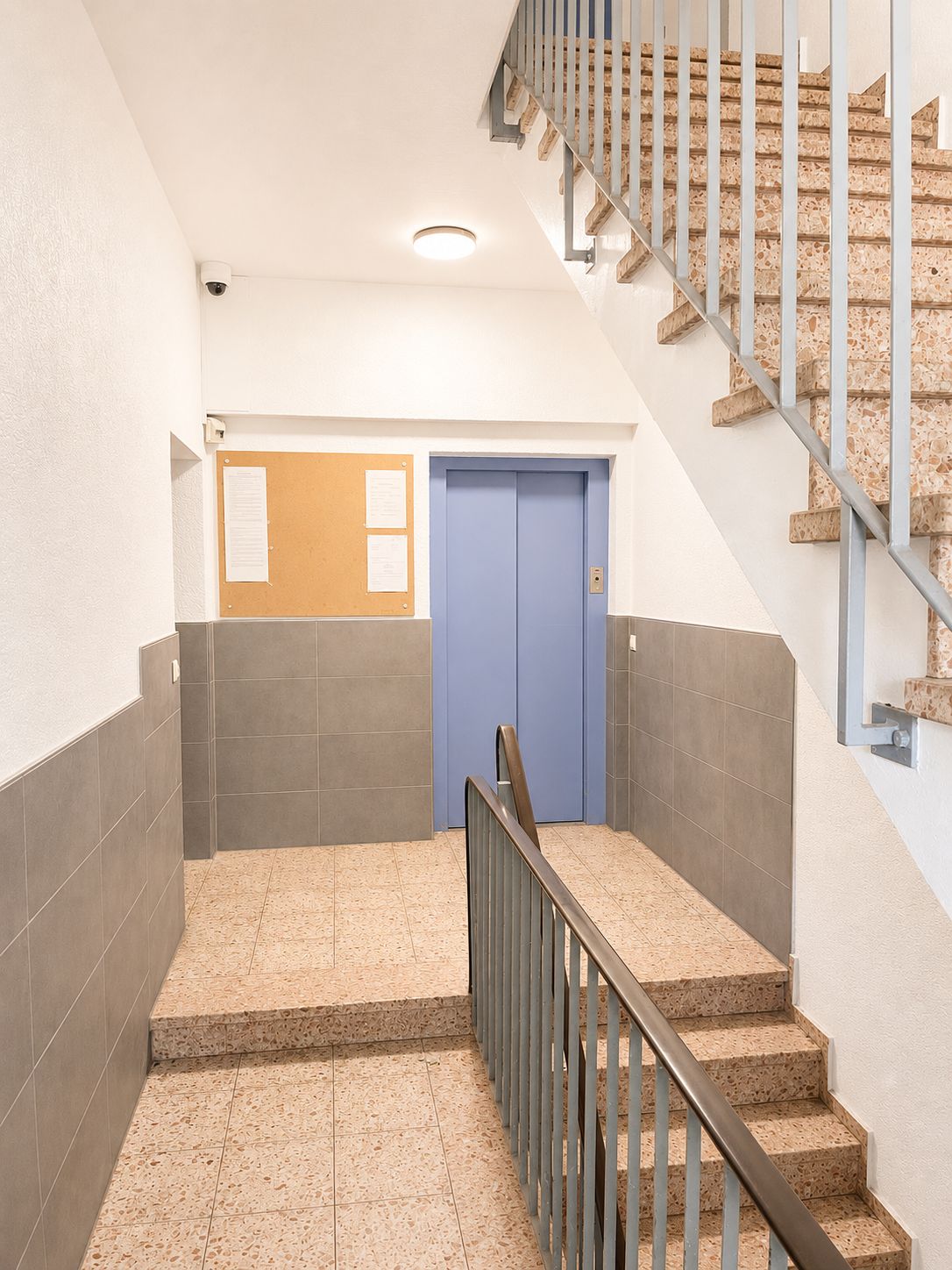 Treppenhaus mit Aufzug, Treppe und Infotafel in einem Wohngebäude.