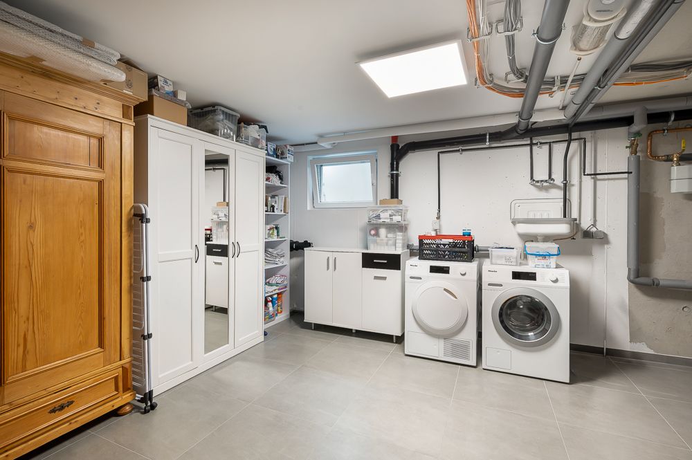 Hauswirtschaftsraum mit Waschmaschine, Trockner, Schränken und Regalen, Rohre an der Decke.