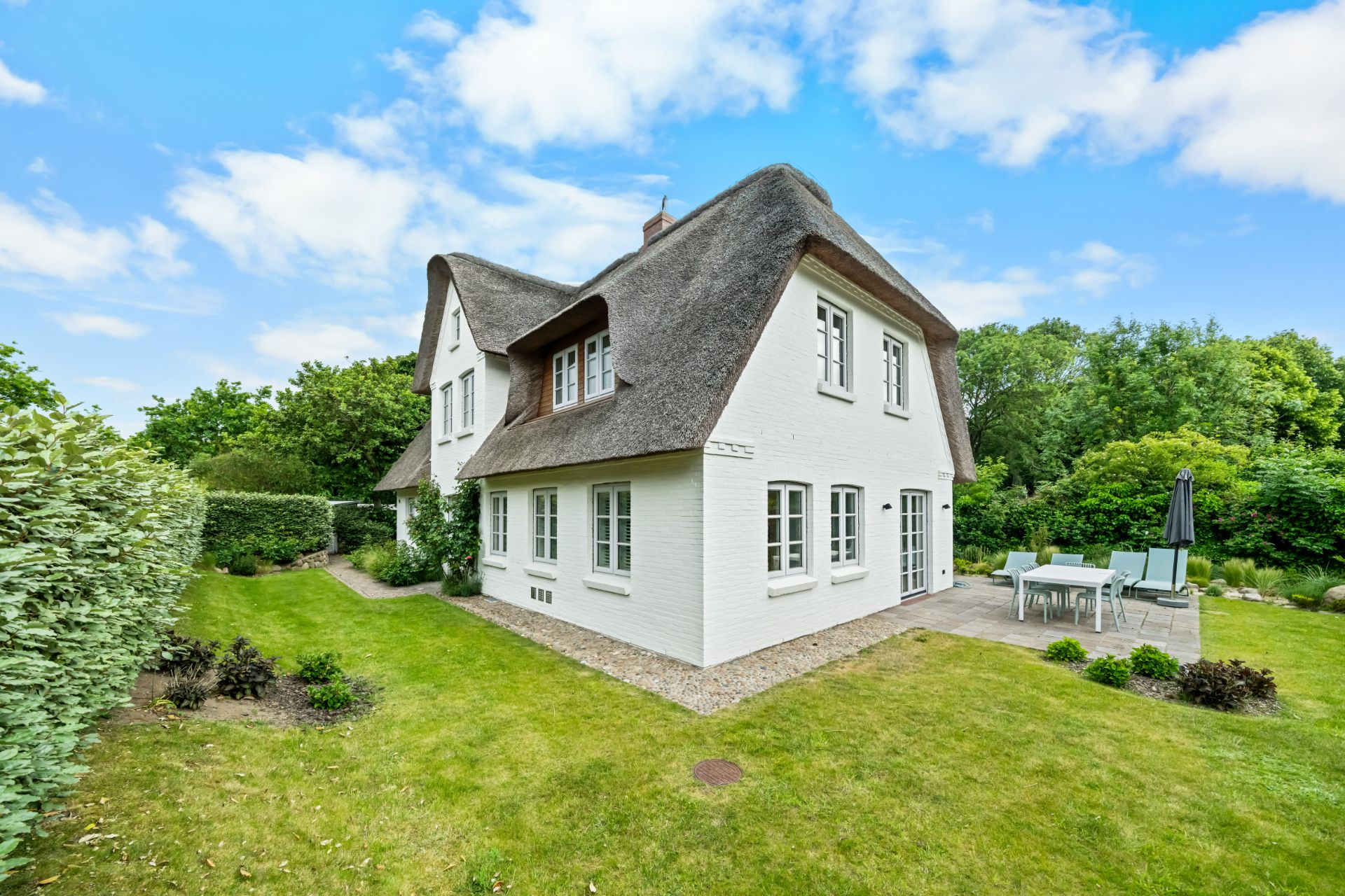 Weißes Haus mit Reetdach, Garten und Terrasse mit Sitzgruppe im Grünen.
