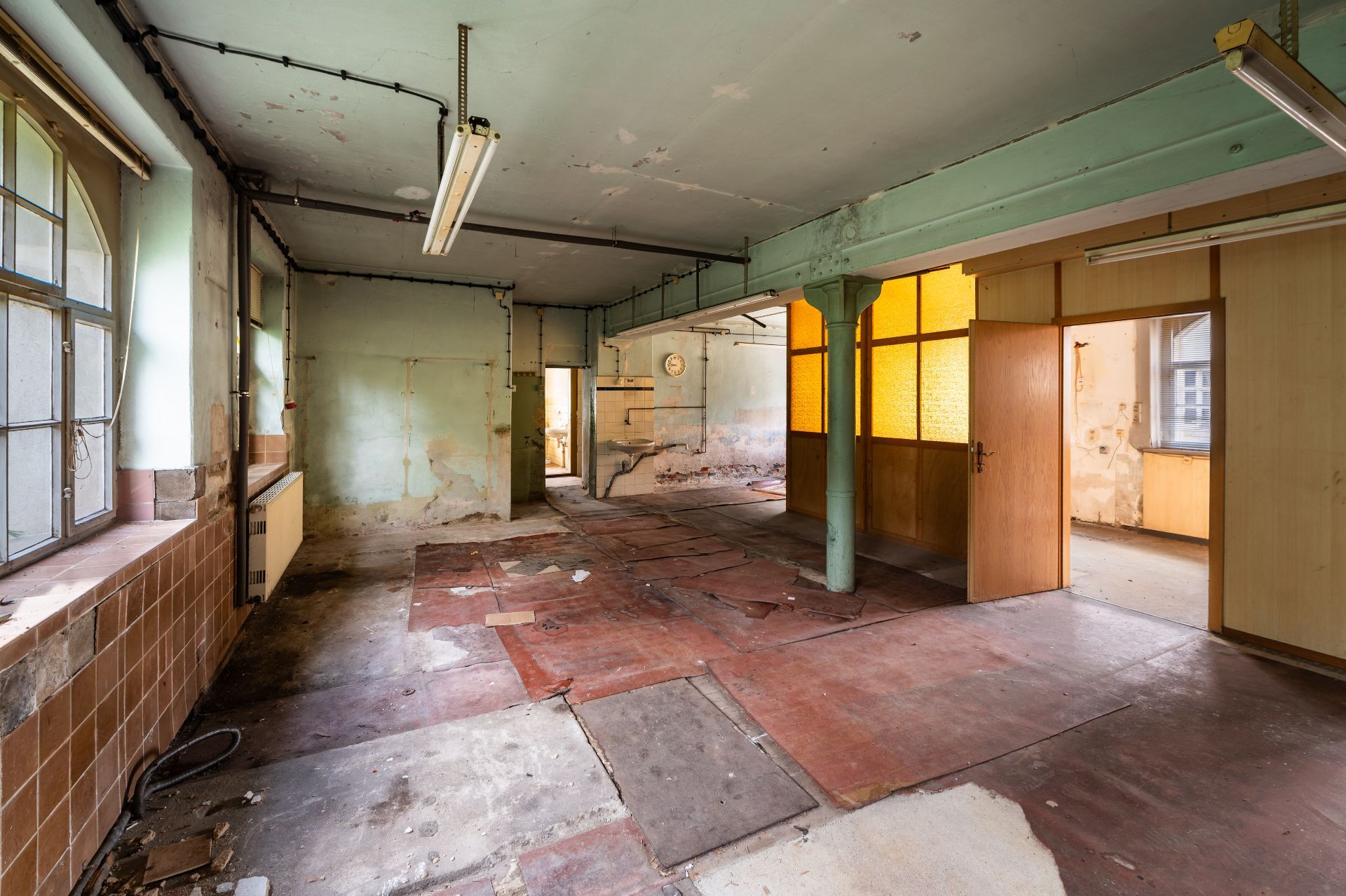 Leeres, abgenutztes Zimmer mit offenem Grundriss, Pfosten, großen Fenstern und offenen Türen.