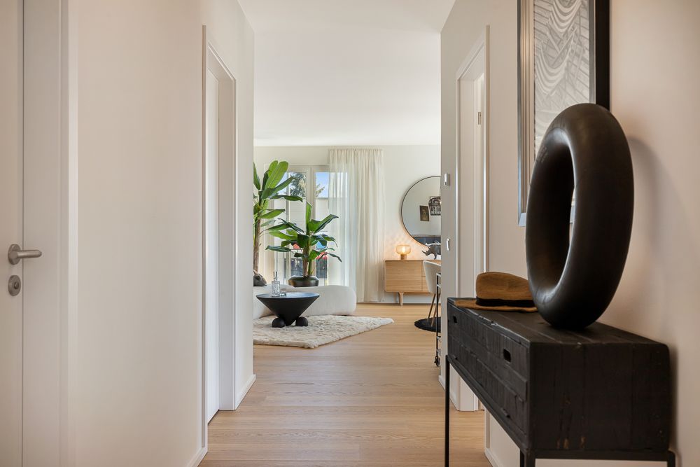 Heller Flur mit Holzboden, Dekotisch, Pflanzen und Blick ins gemütliche Wohnzimmer.