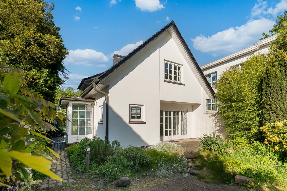 Weißes Einfamilienhaus mit Garten, großen Fenstern und Gartenweg bei sonnigem Wetter.