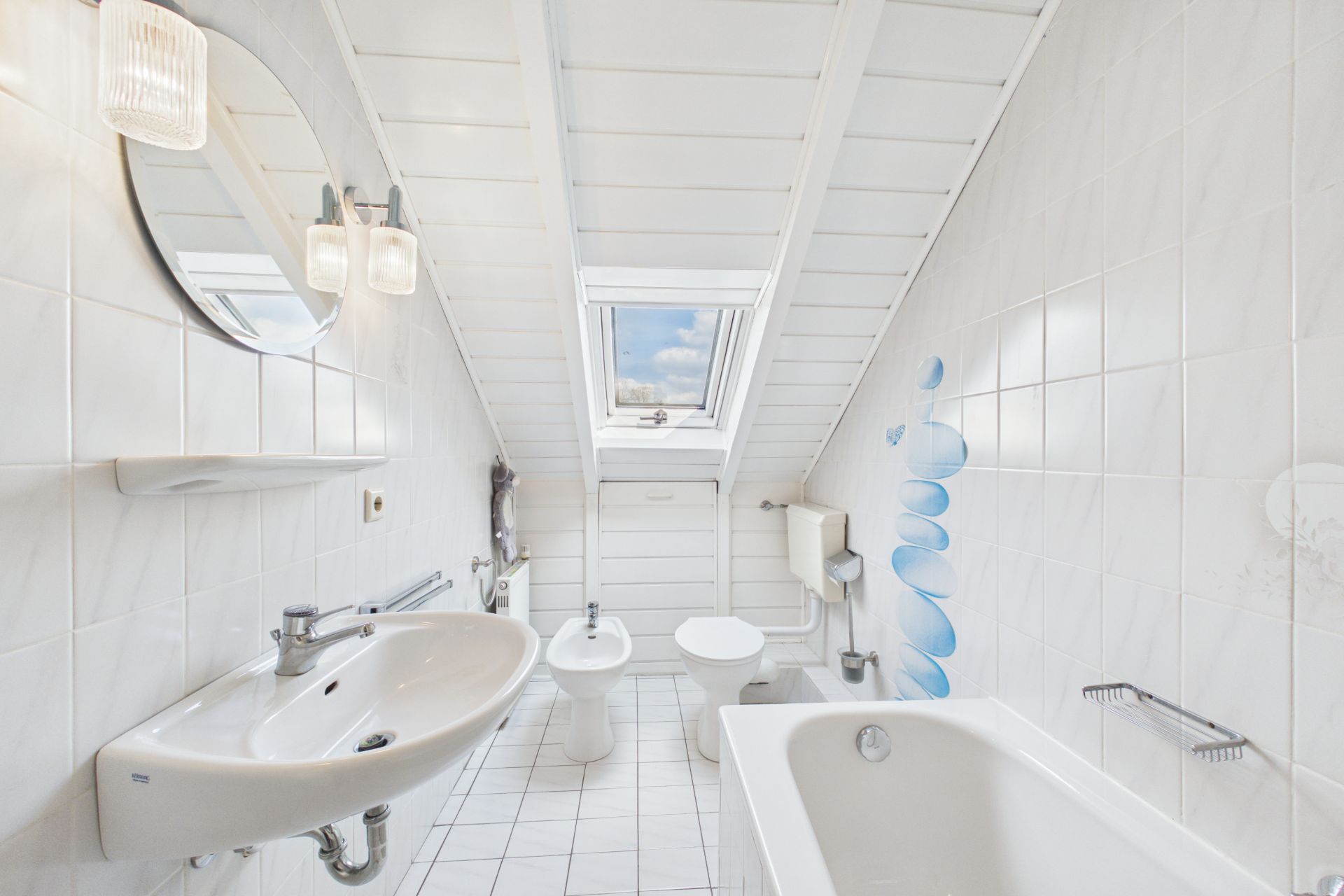 Helles Badezimmer mit Dachfenster, Waschbecken, Badewanne, Toilette und Bidet.